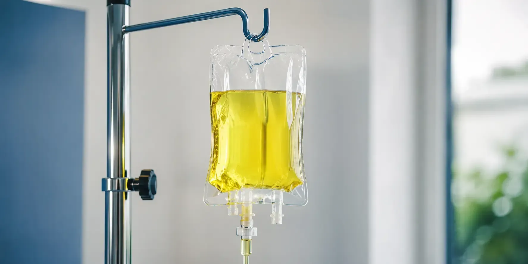 Close-up of a mobile IV drip therapy bag filled with bright yellow vitamin infusion hanging from a sleek medical pole in a clean clinical setting, representing convenient wellness and hydration treatment.