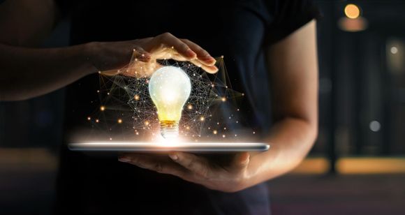 Personne tenant une tablette, une ampoule lumineuse en lévitation au-dessus, un réseau de connexions autour d'elle.