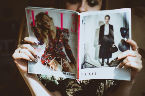 Femme tenant le magazine ELLE ouvert, avec un mannequin en robe fleurie et un deuxième mannequin en noir.
