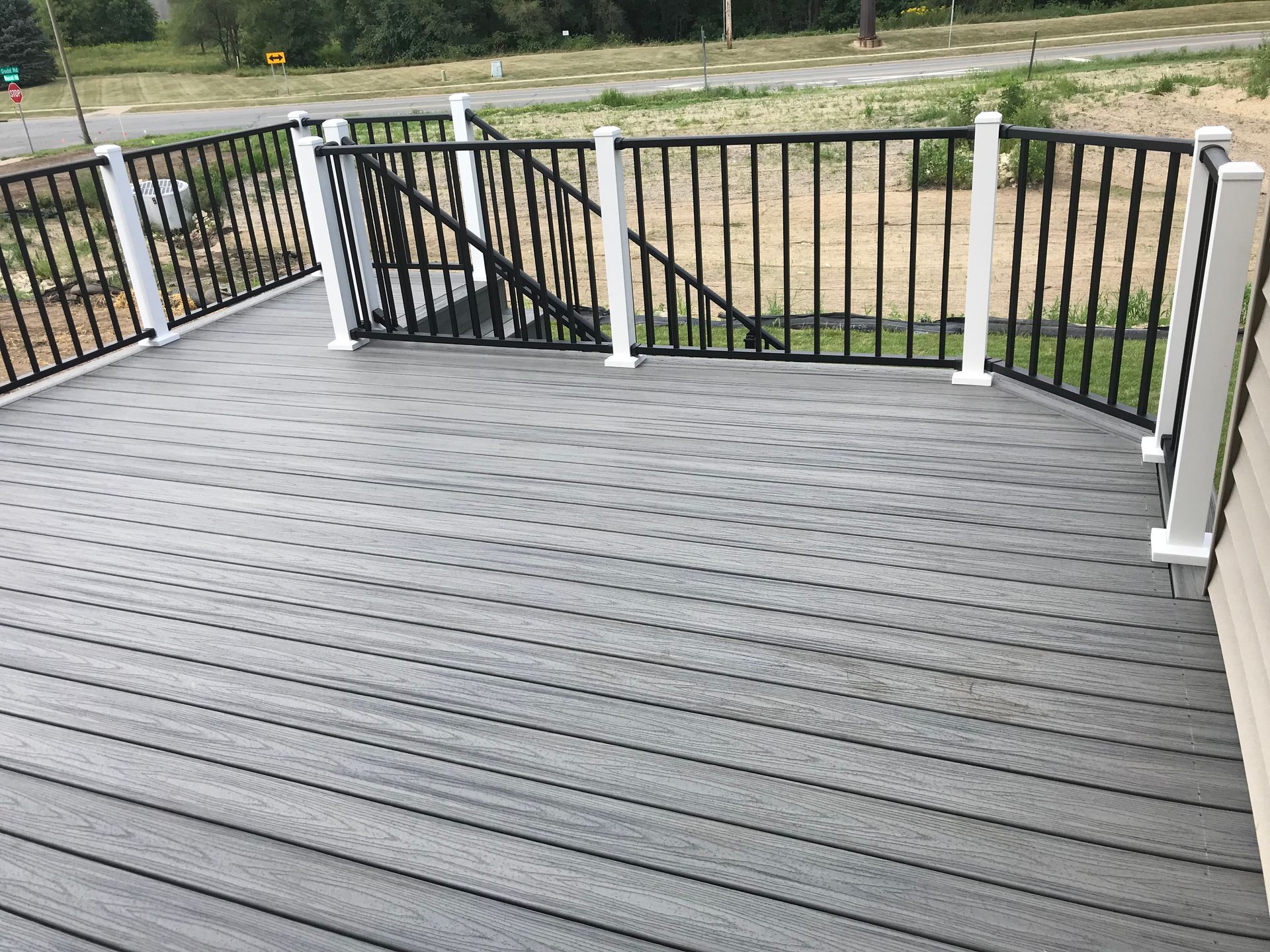 Gray deck overlooking a fenced yard with black metal and white railings.