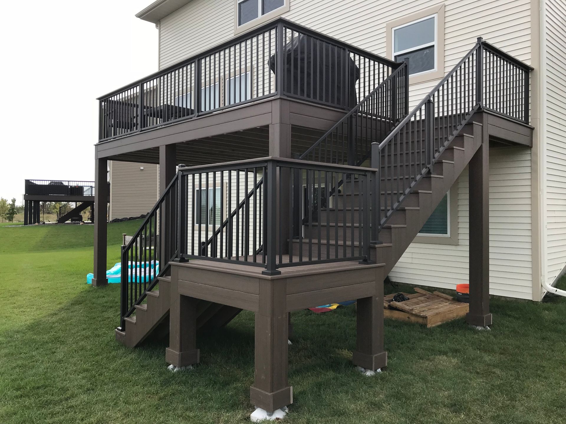 Backyard deck with stairs and black railings on a two-story house