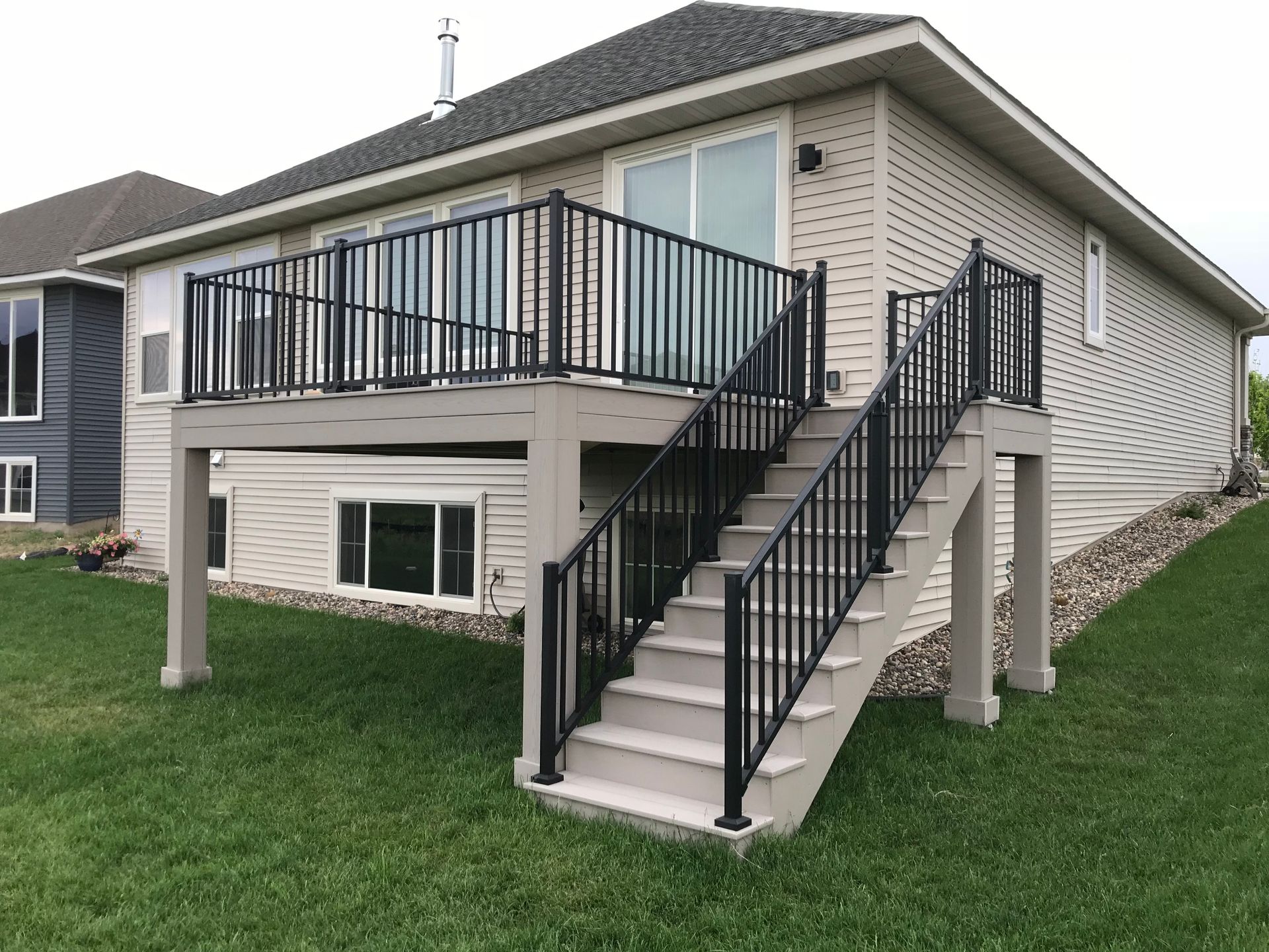 Backyard view of a raised deck with black railings and stairs on a beige house