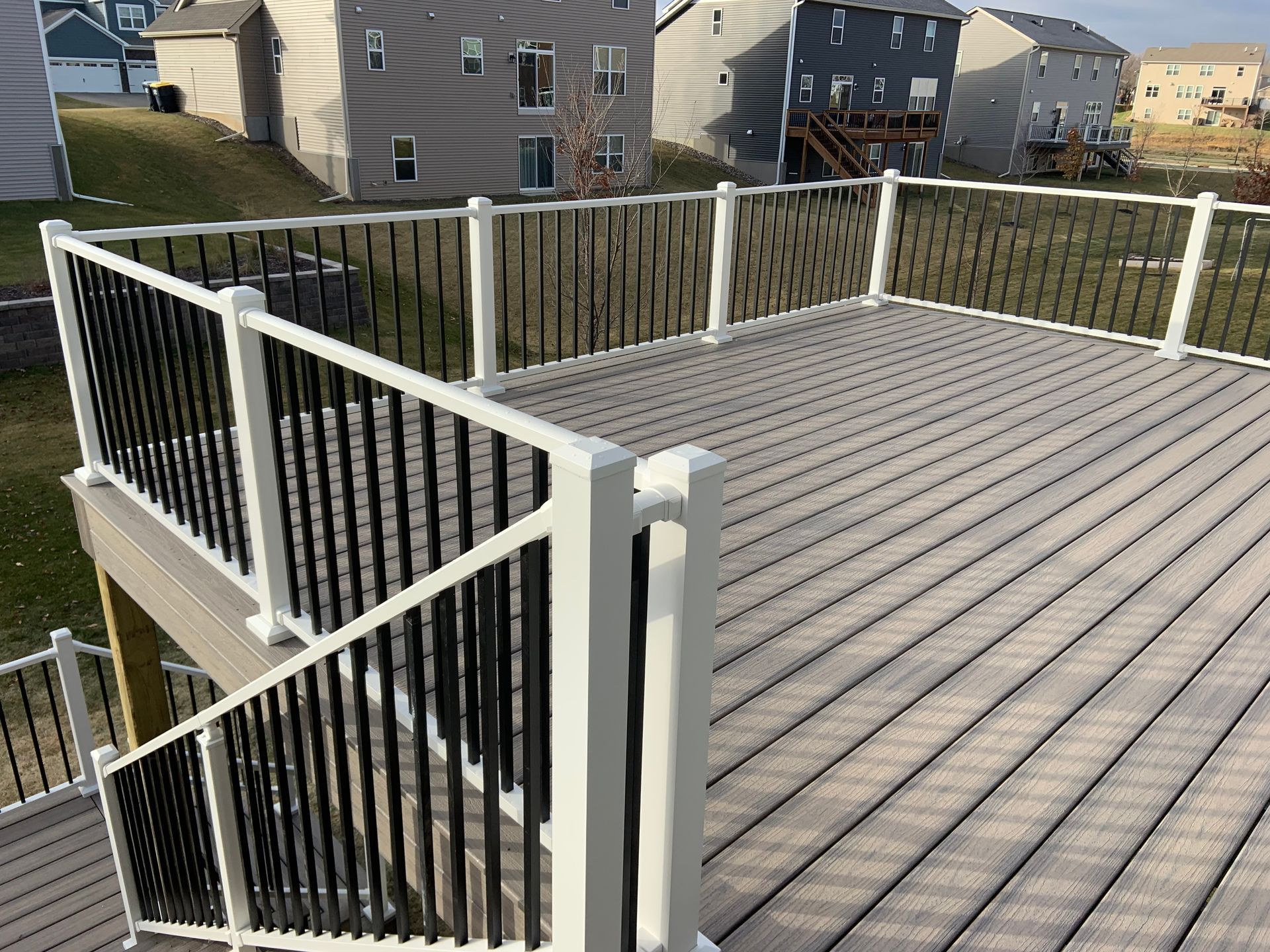 Rooftop deck with gray composite flooring and white railing overlooking neighboring houses.