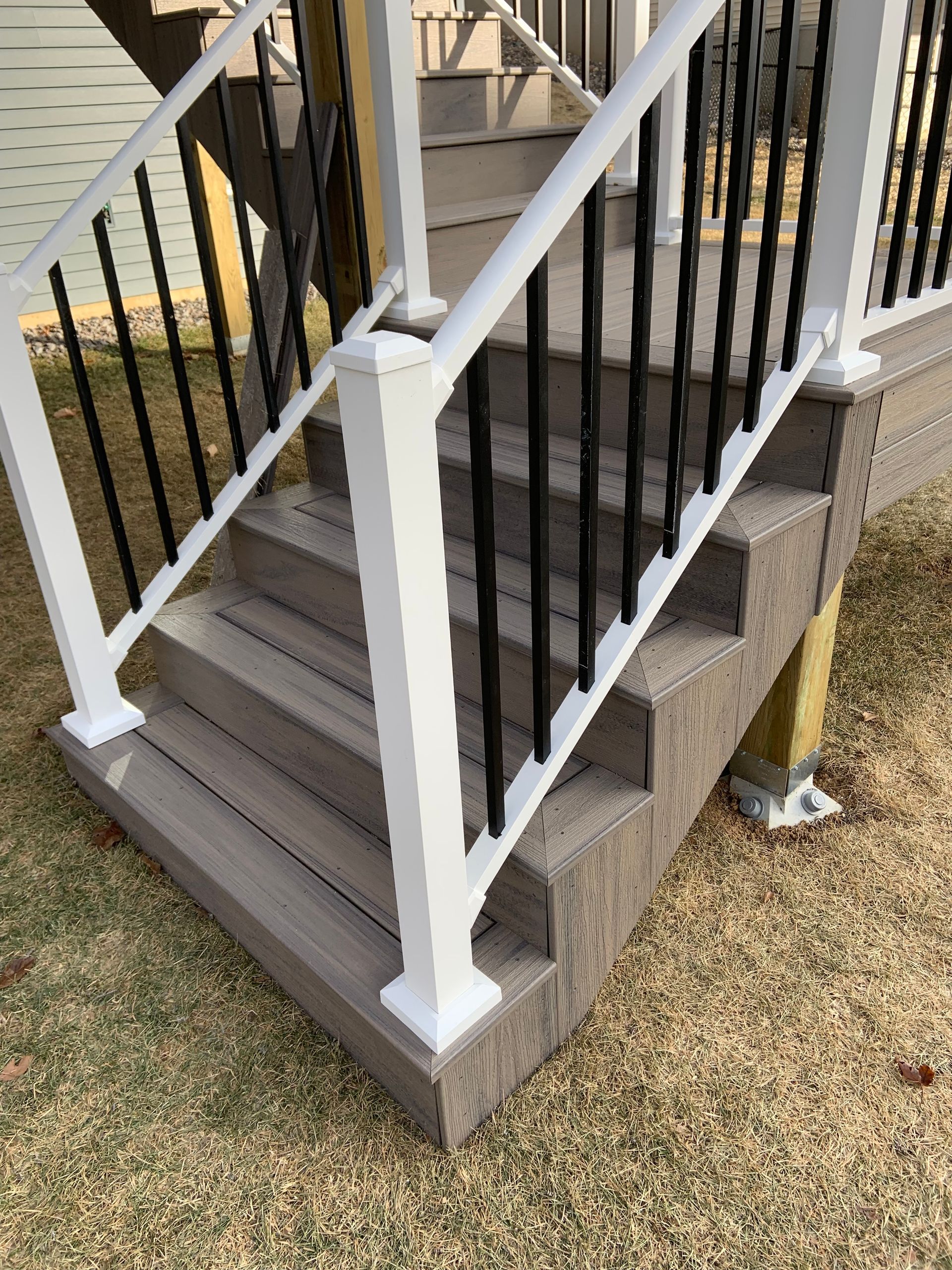 Front porch stairs with white railings, black balusters, and gray stone steps beside grass.