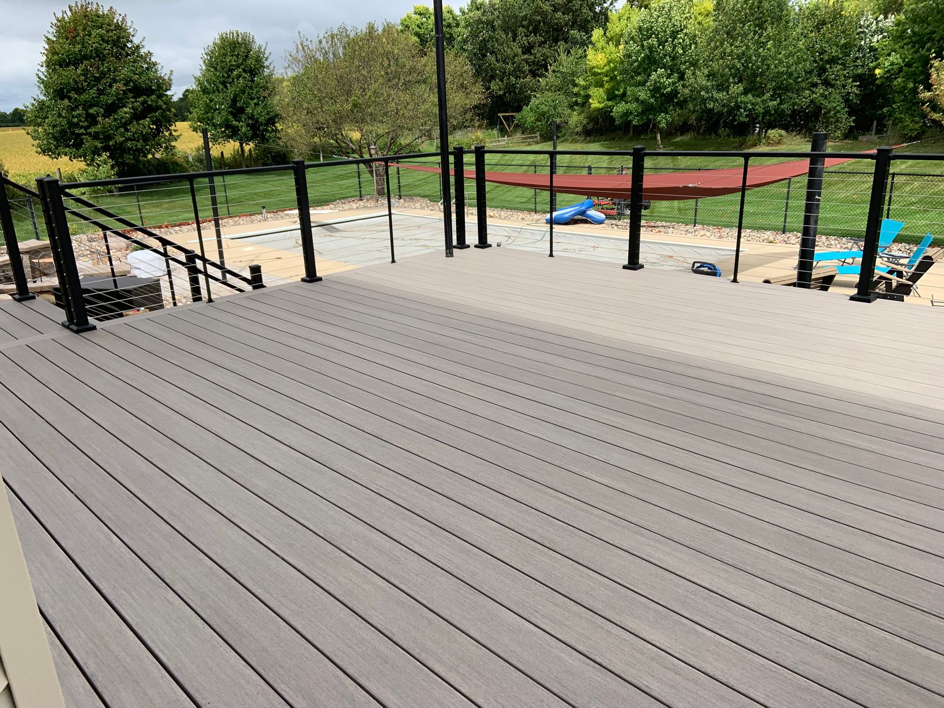 Empty wooden deck overlooking a fenced outdoor area with sand and playground equipment.