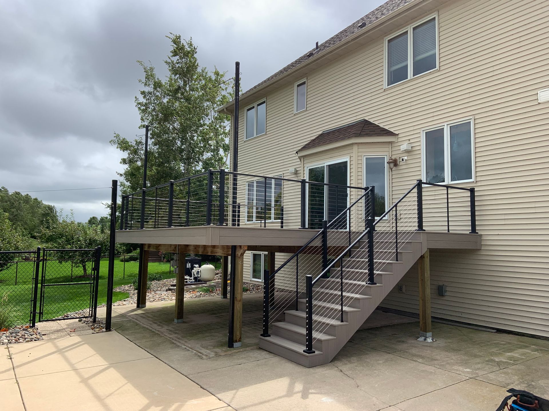 Back deck with stairs on a beige house, black railings, and cloudy sky