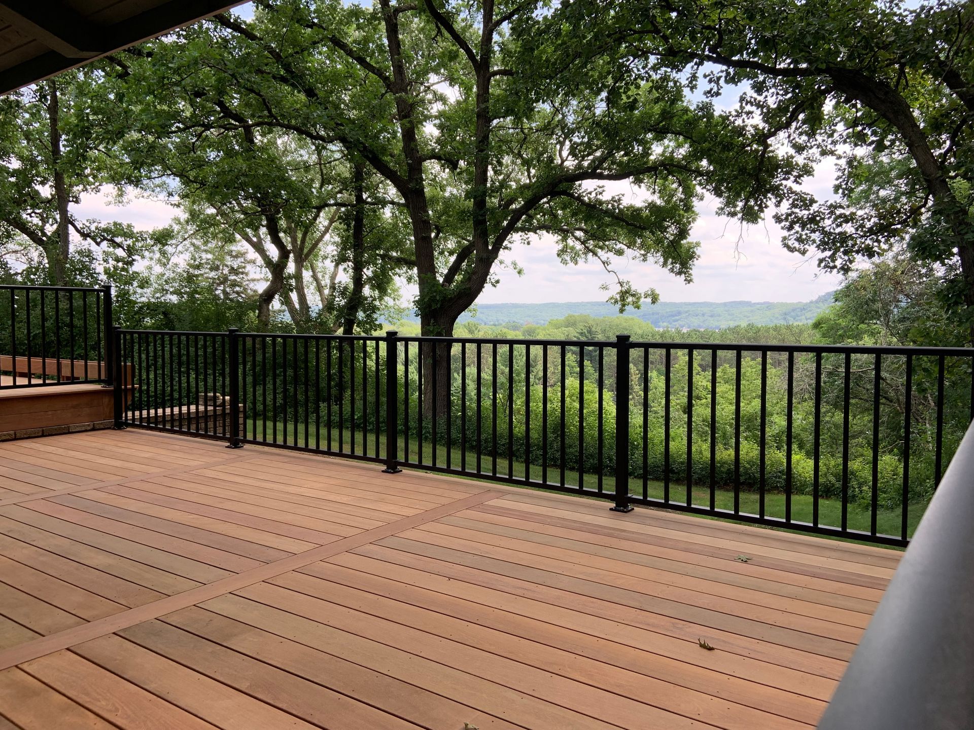 Wooden deck with black railing overlooking green trees and a distant landscape