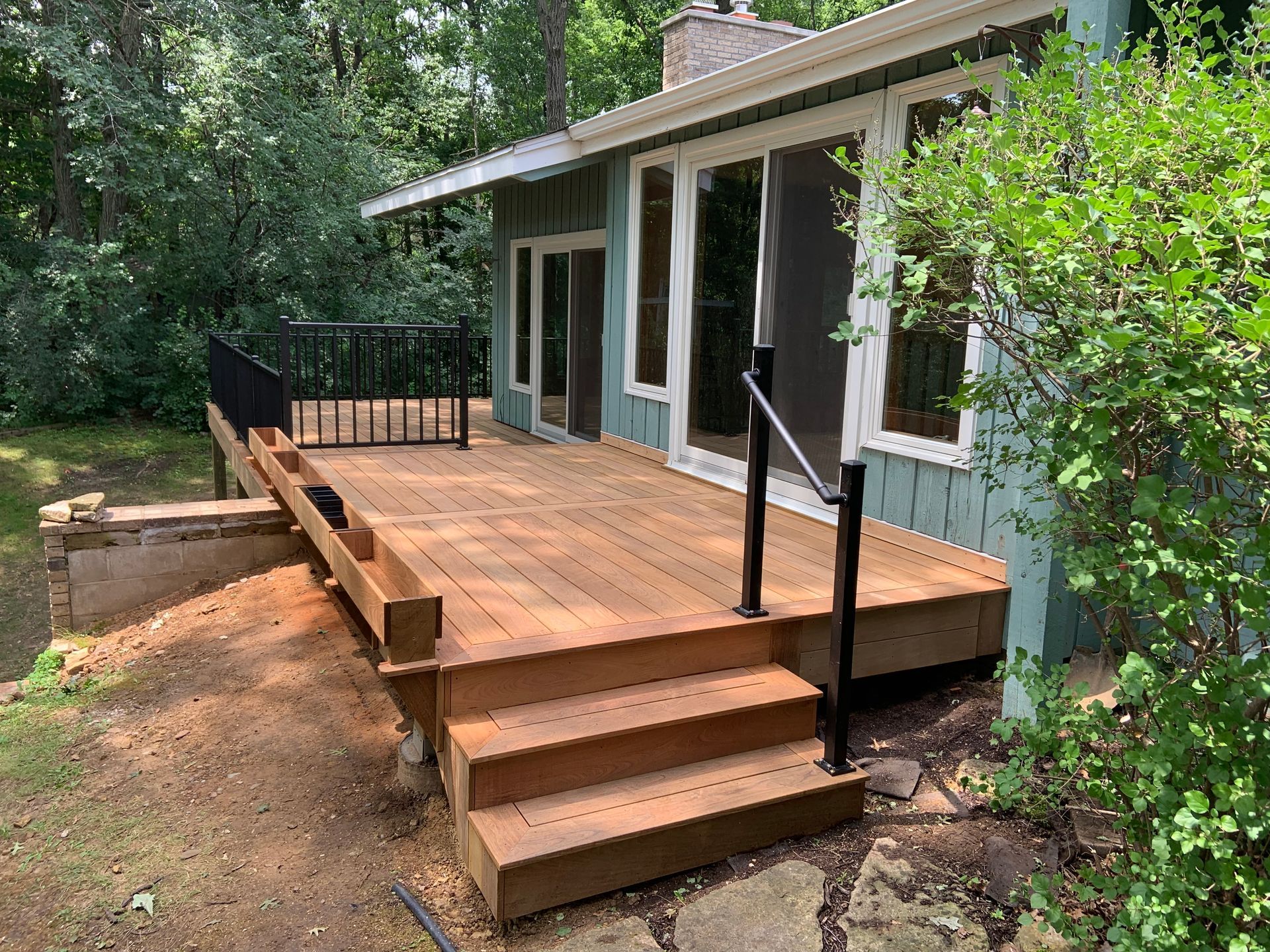 Wooden accessibility ramp with steps leading to a house deck surrounded by trees