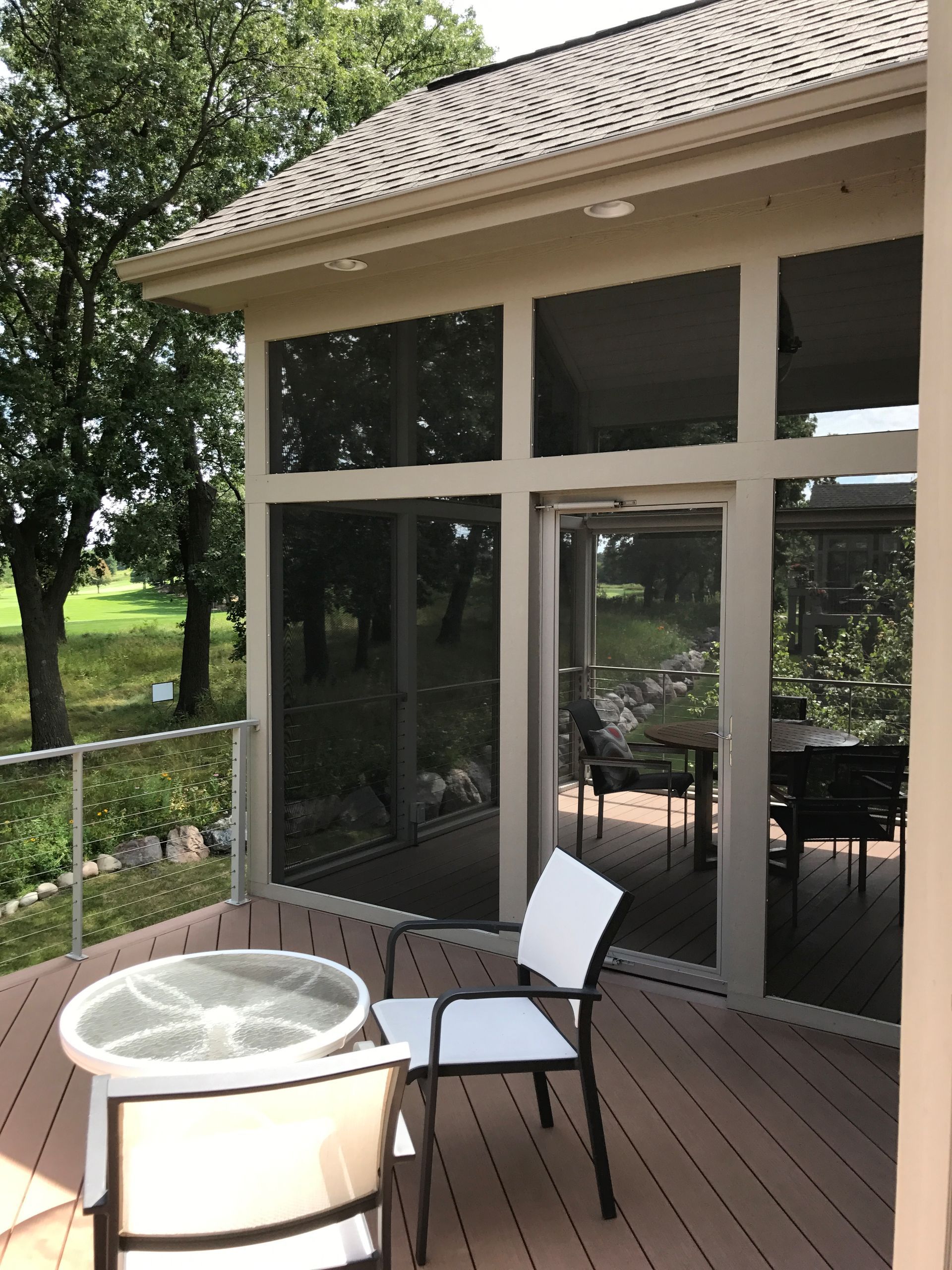 Covered patio with glass doors, patio chairs, and a round fire pit table beside a grassy yard