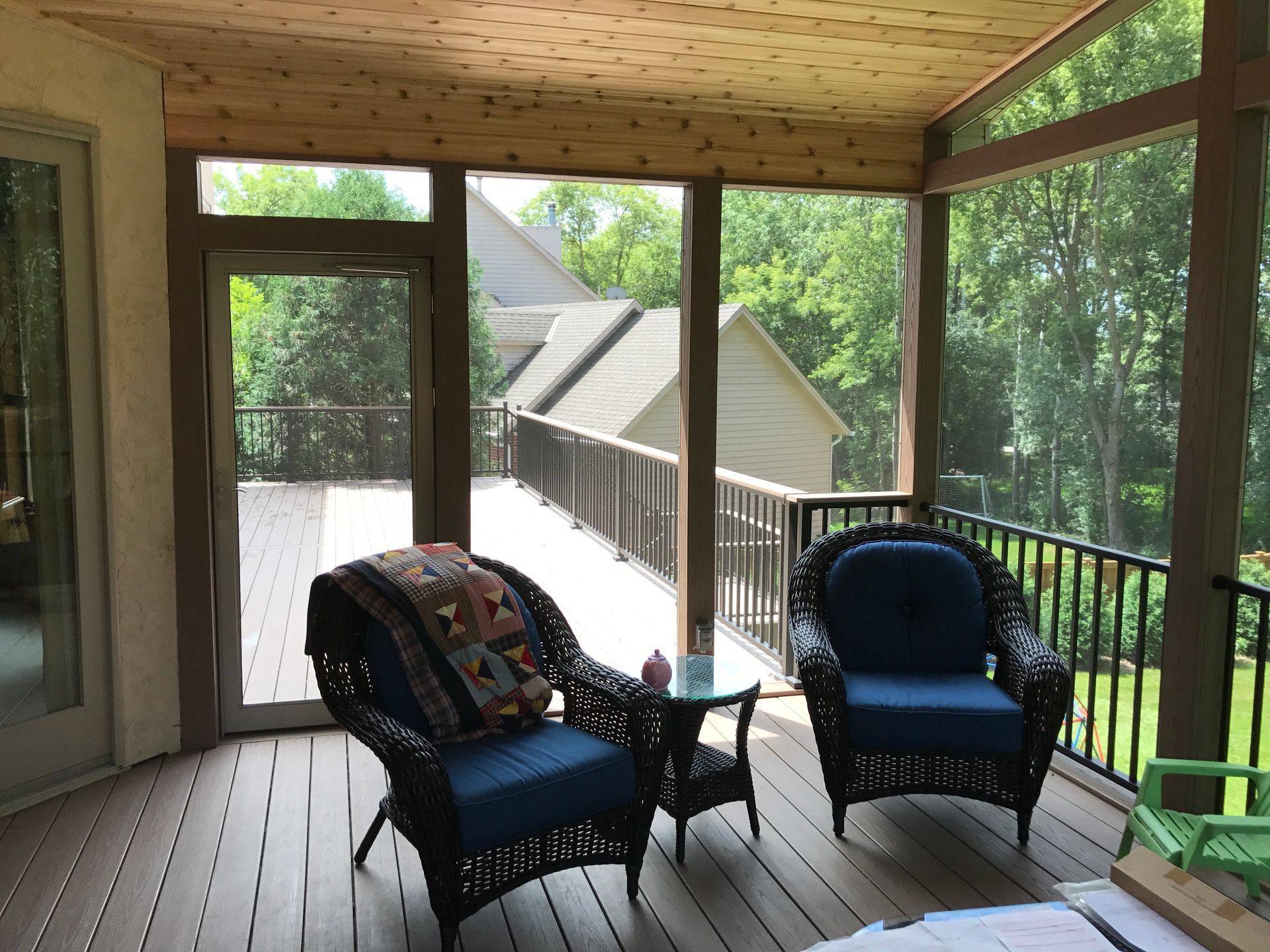 Covered wooden porch with two blue chairs, a small table, and a view of the wooded hillside beyond.