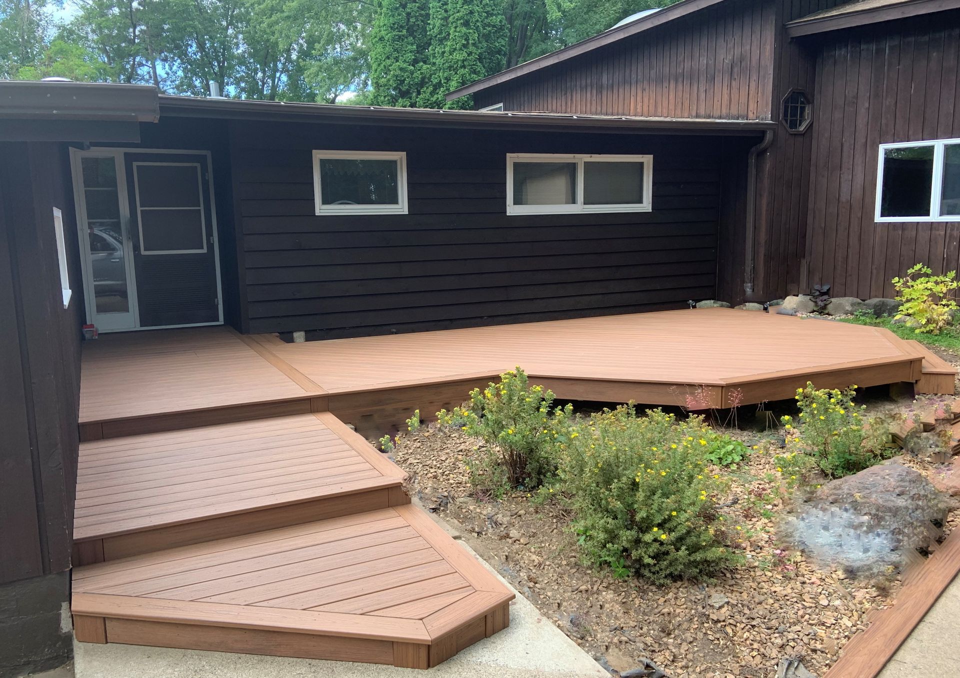 Wooden house deck with steps, small windows, and a gravel garden path in front