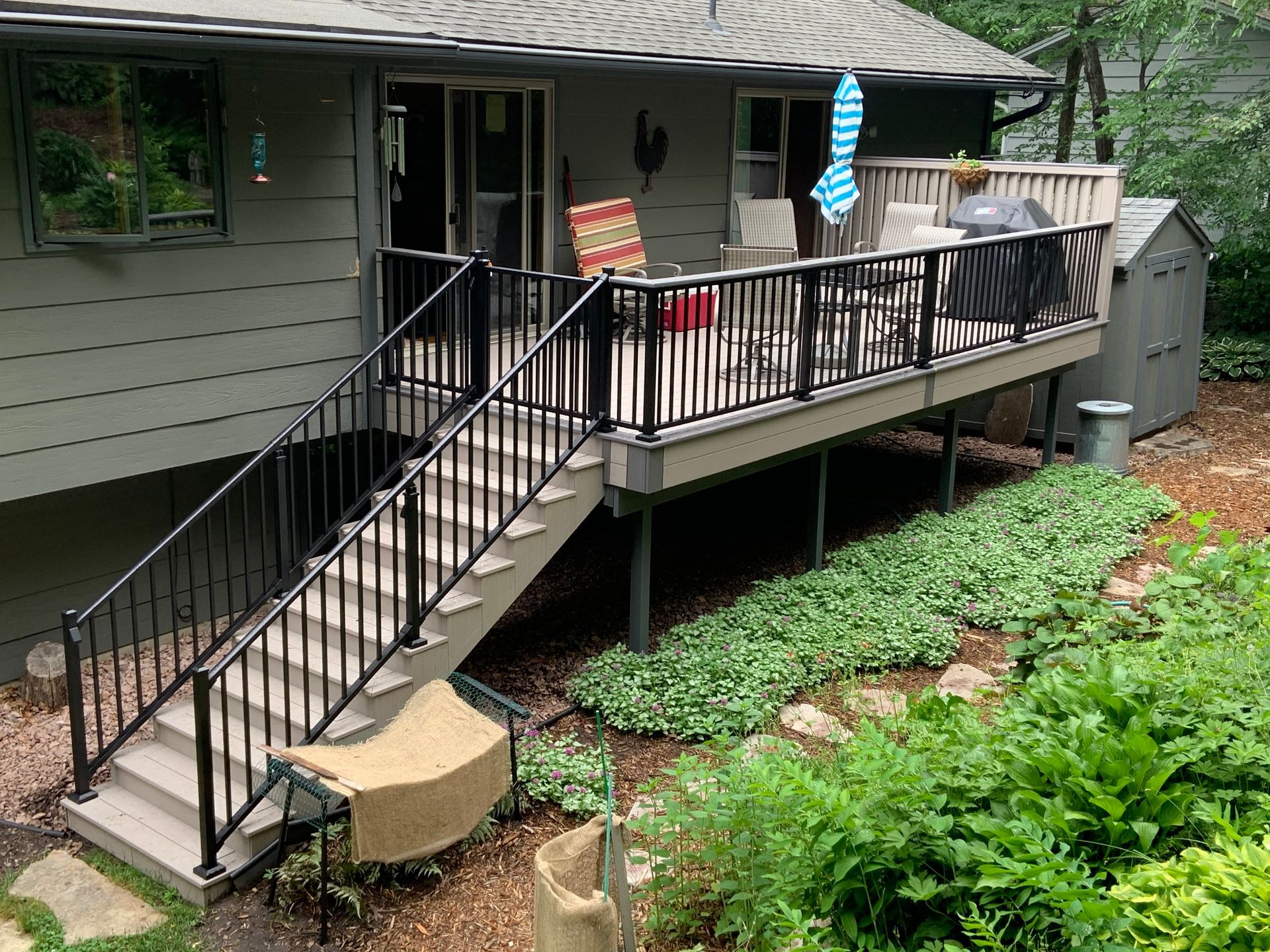 Back porch deck with black railing, stairs, patio furniture, and garden beds beside a house
