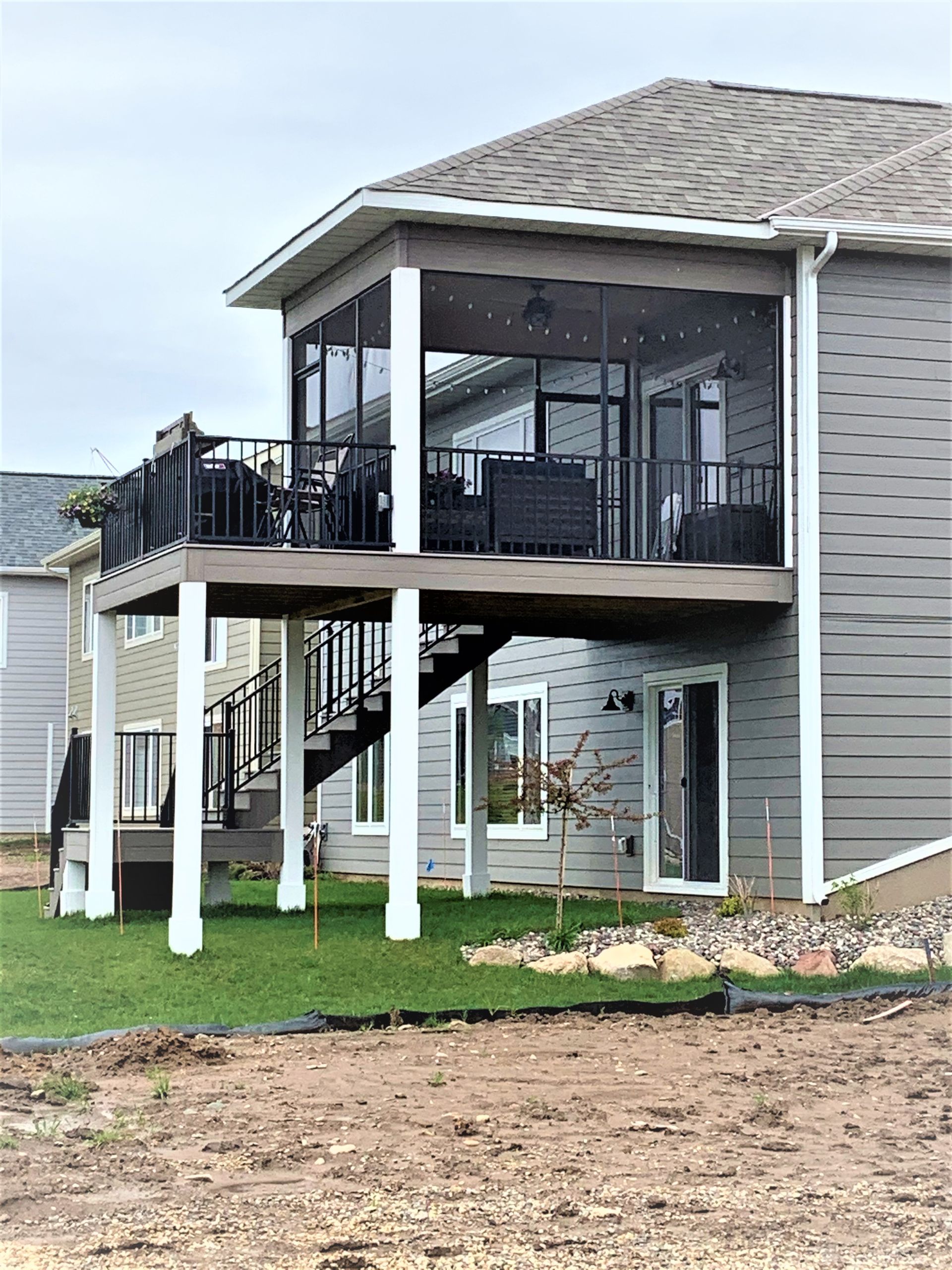 Two-story gray house with a raised screened porch and stairs over a grassy yard
