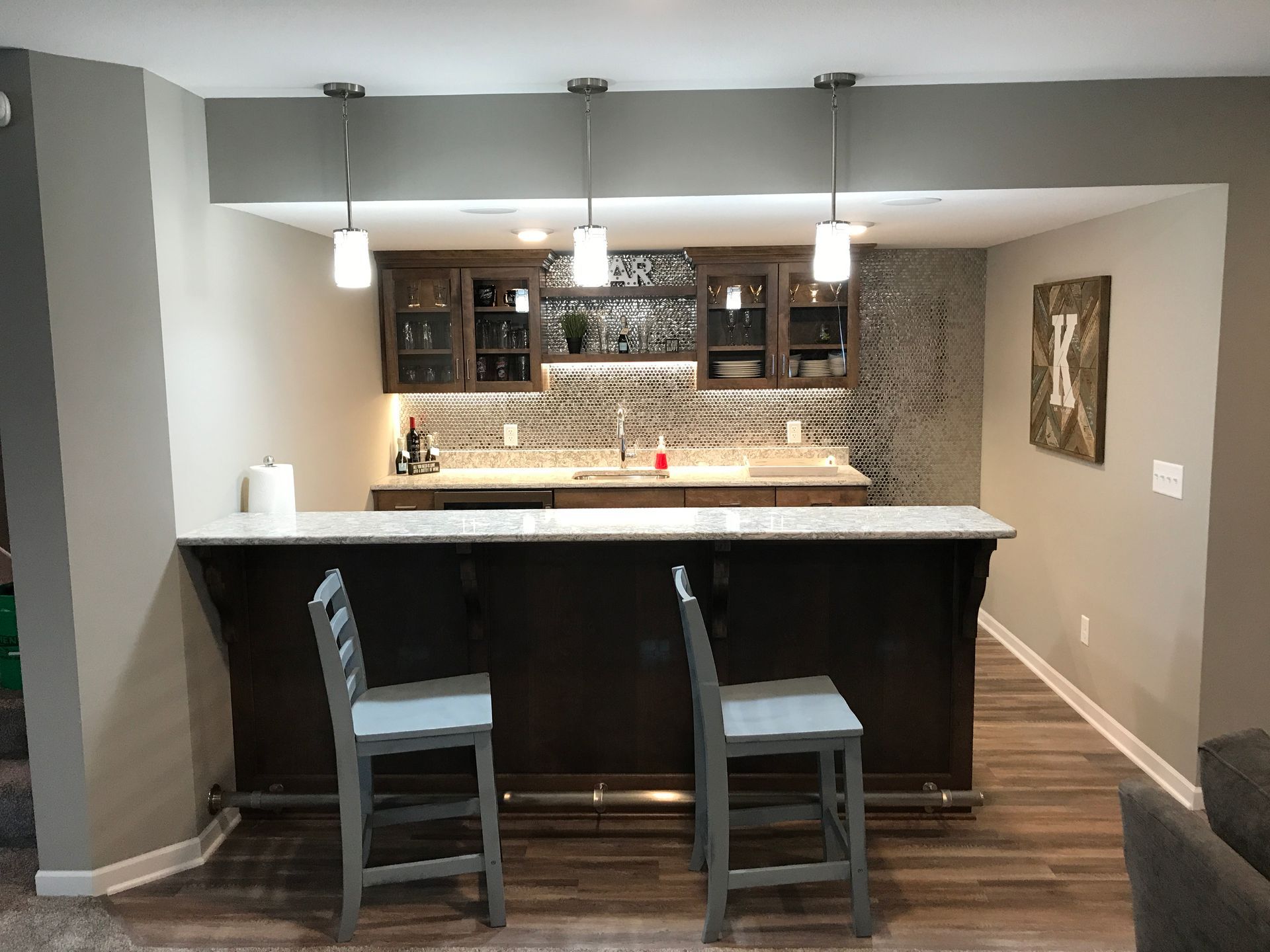 Basement home bar with dark wood counter, two stools, pendant lights, and built-in shelves