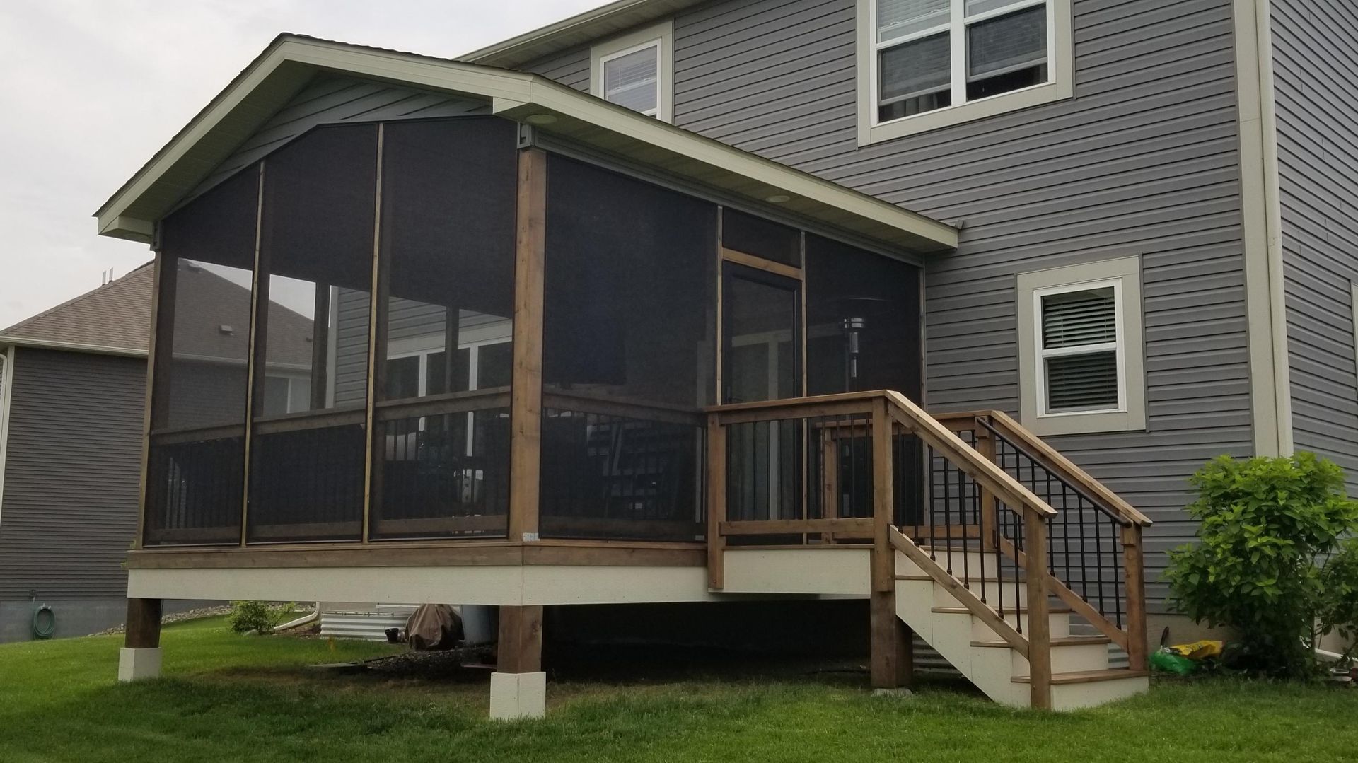 Screened porch with wooden deck and stairs attached to a gray house