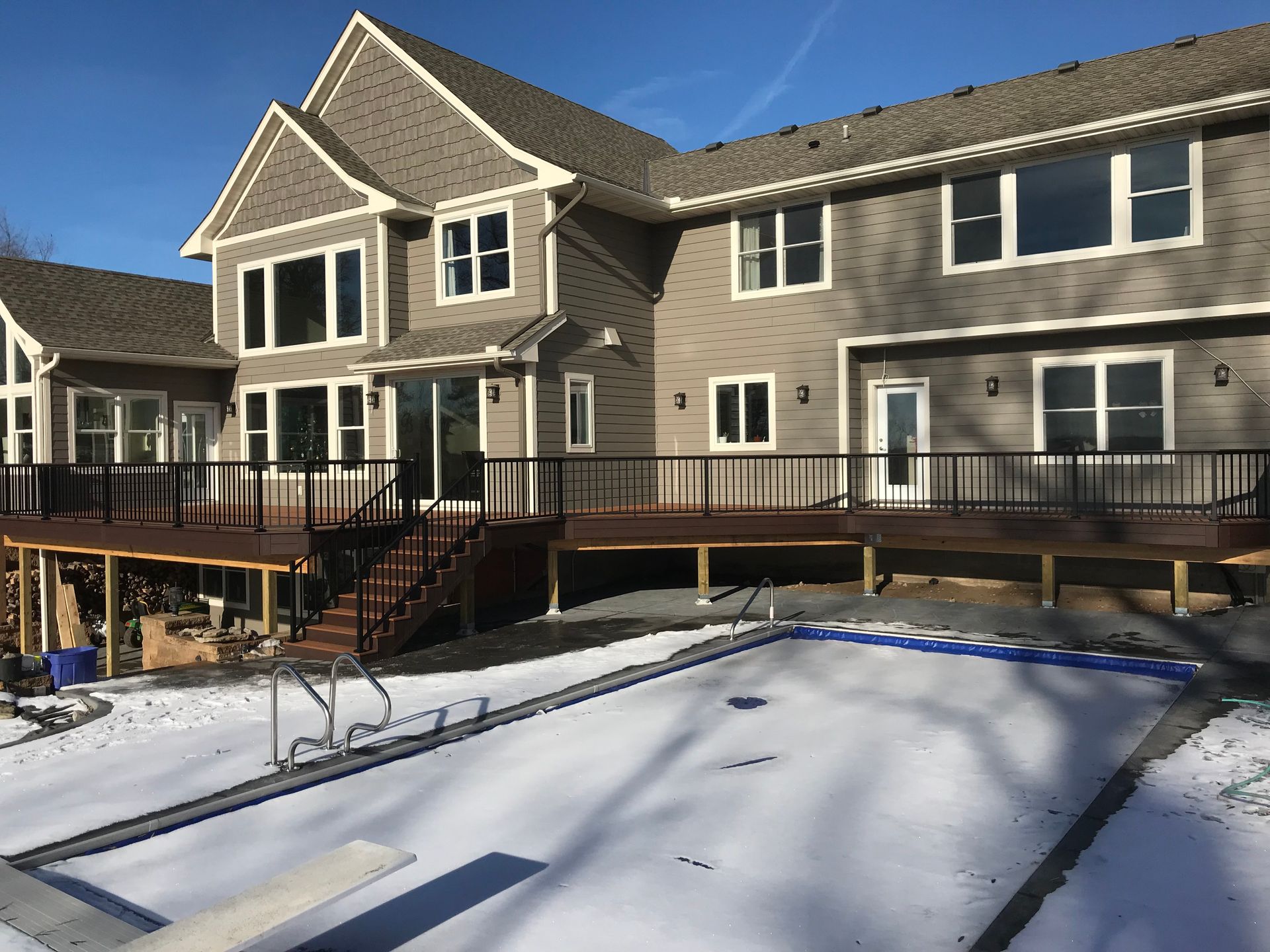 Snowy backyard with an above-ground pool beside a large two-story house and wooden deck