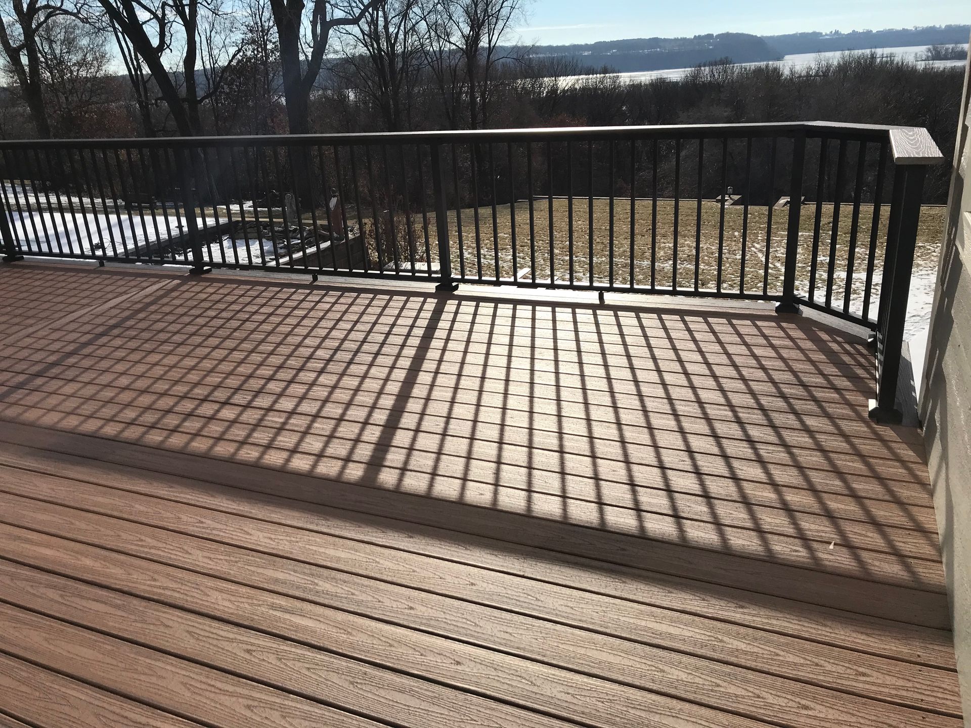 Wooden deck with black metal railing overlooking a snowy landscape and distant water.