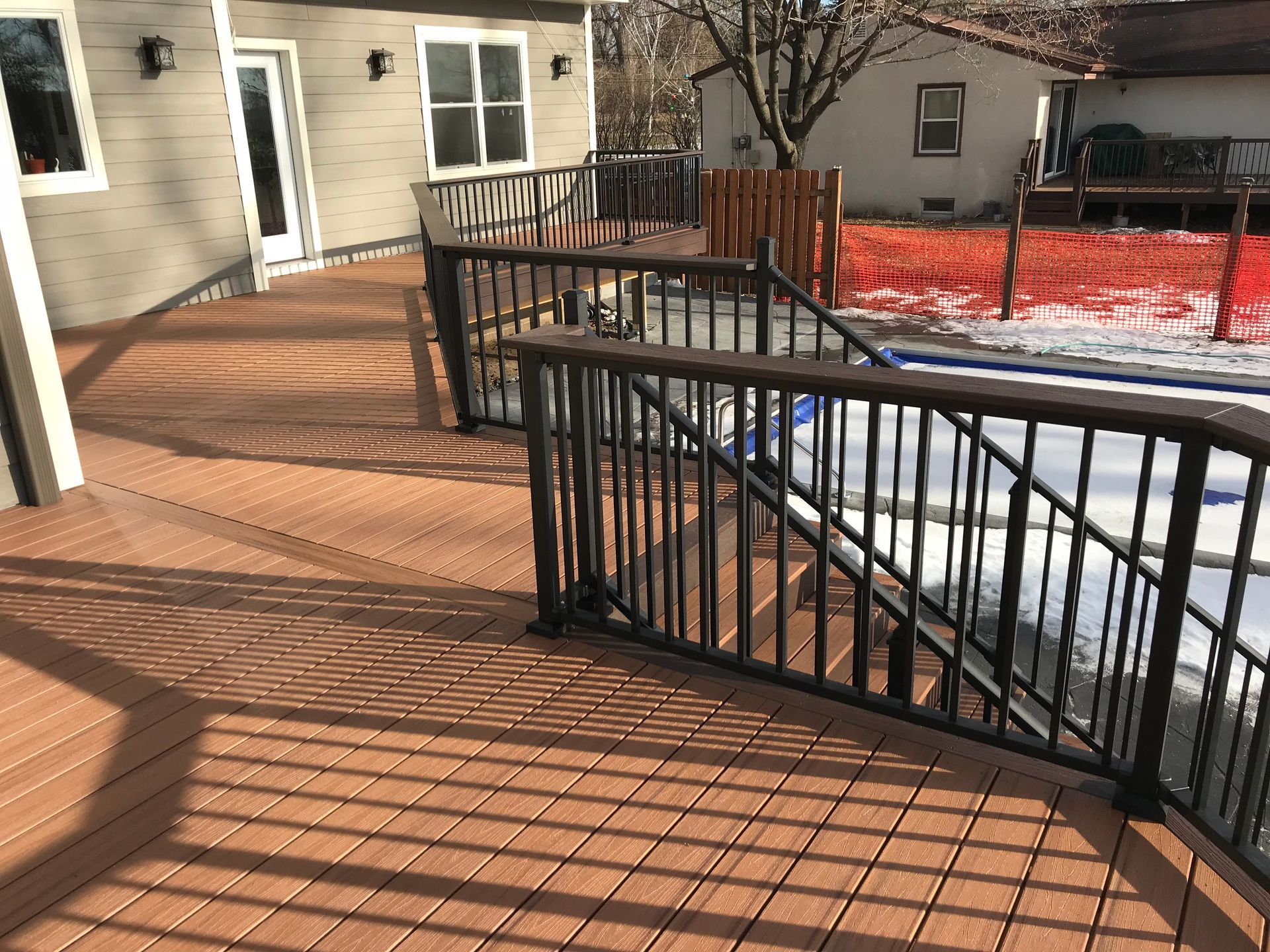 Snowy wooden deck with black railings outside a beige apartment building