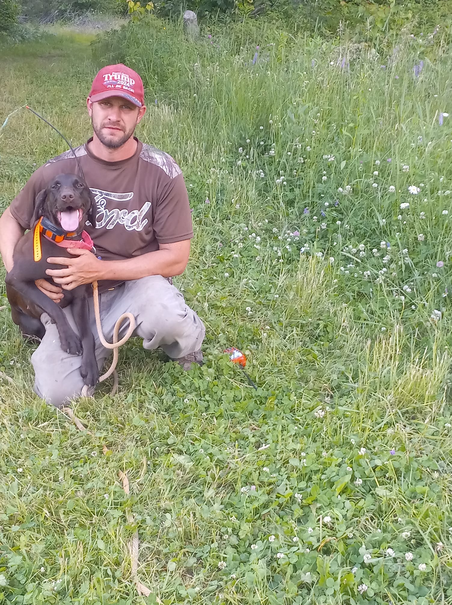 A man is kneeling down in the grass holding a puppy.