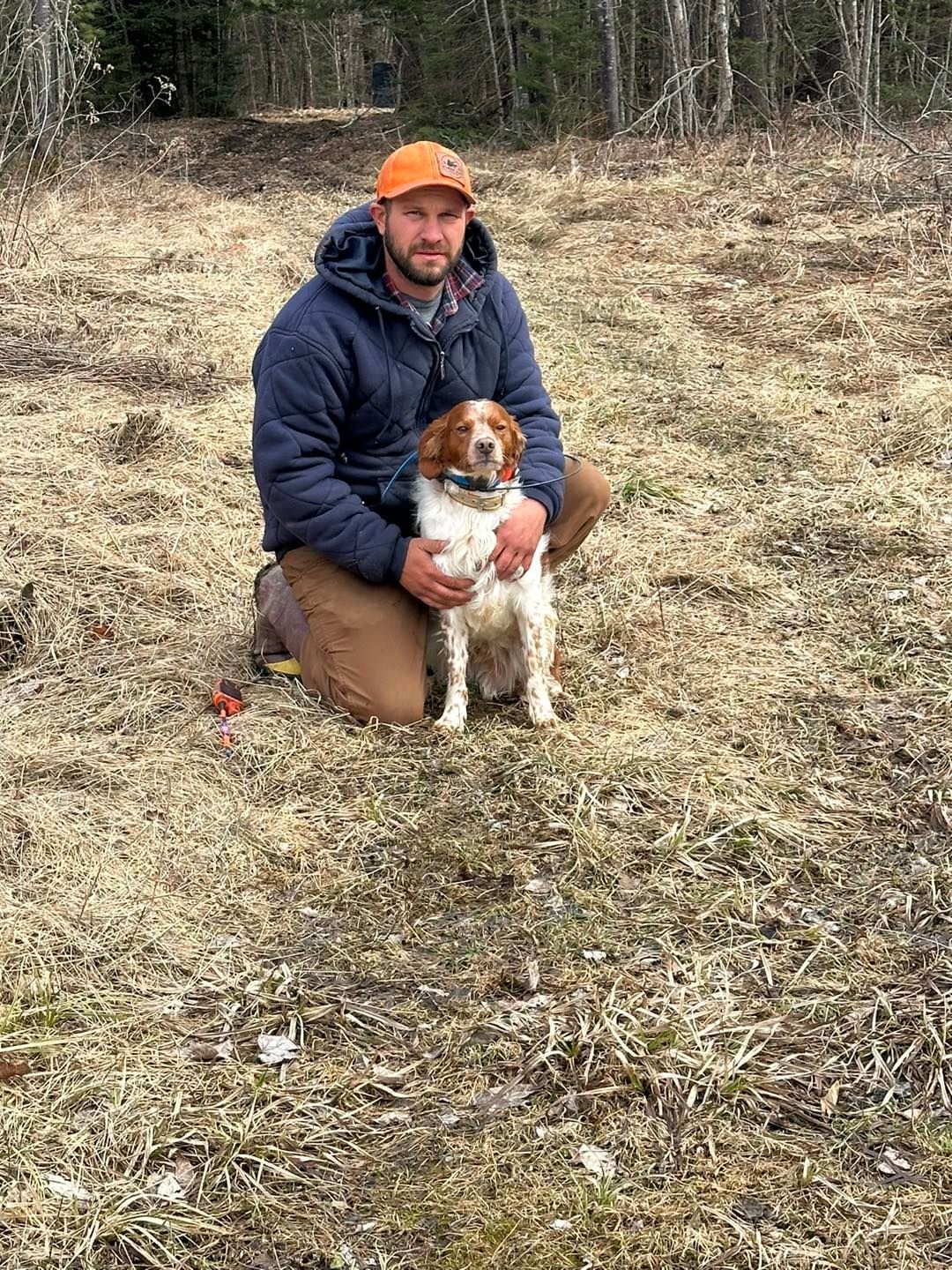 A man is kneeling down next to a dog in a field.