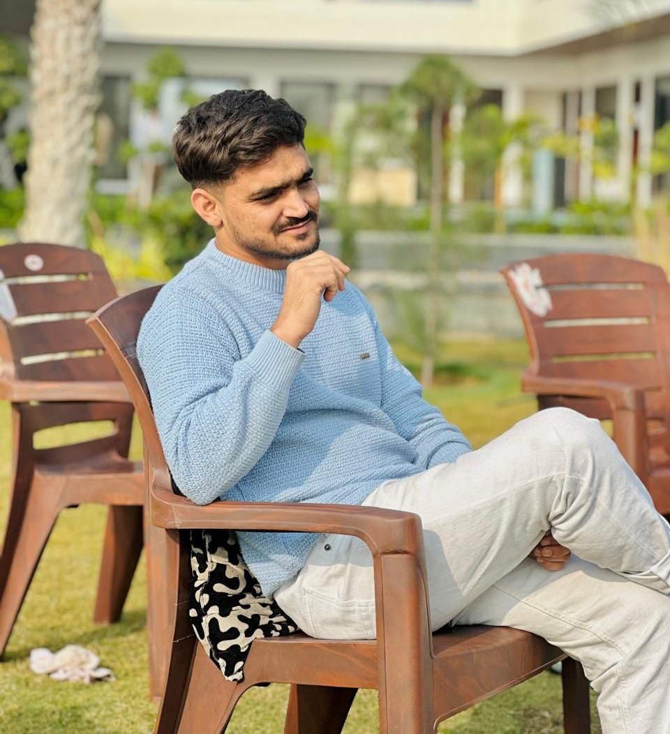 A man is sitting at a table holding a cup of coffee and using a laptop computer.