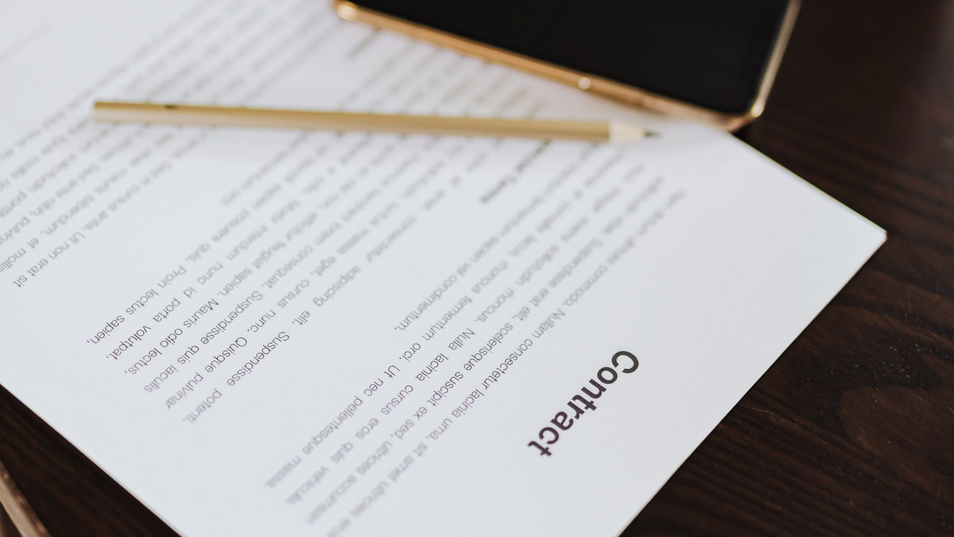 Contract document on a wooden desk with glasses case, pen, and pencil alongside pages.