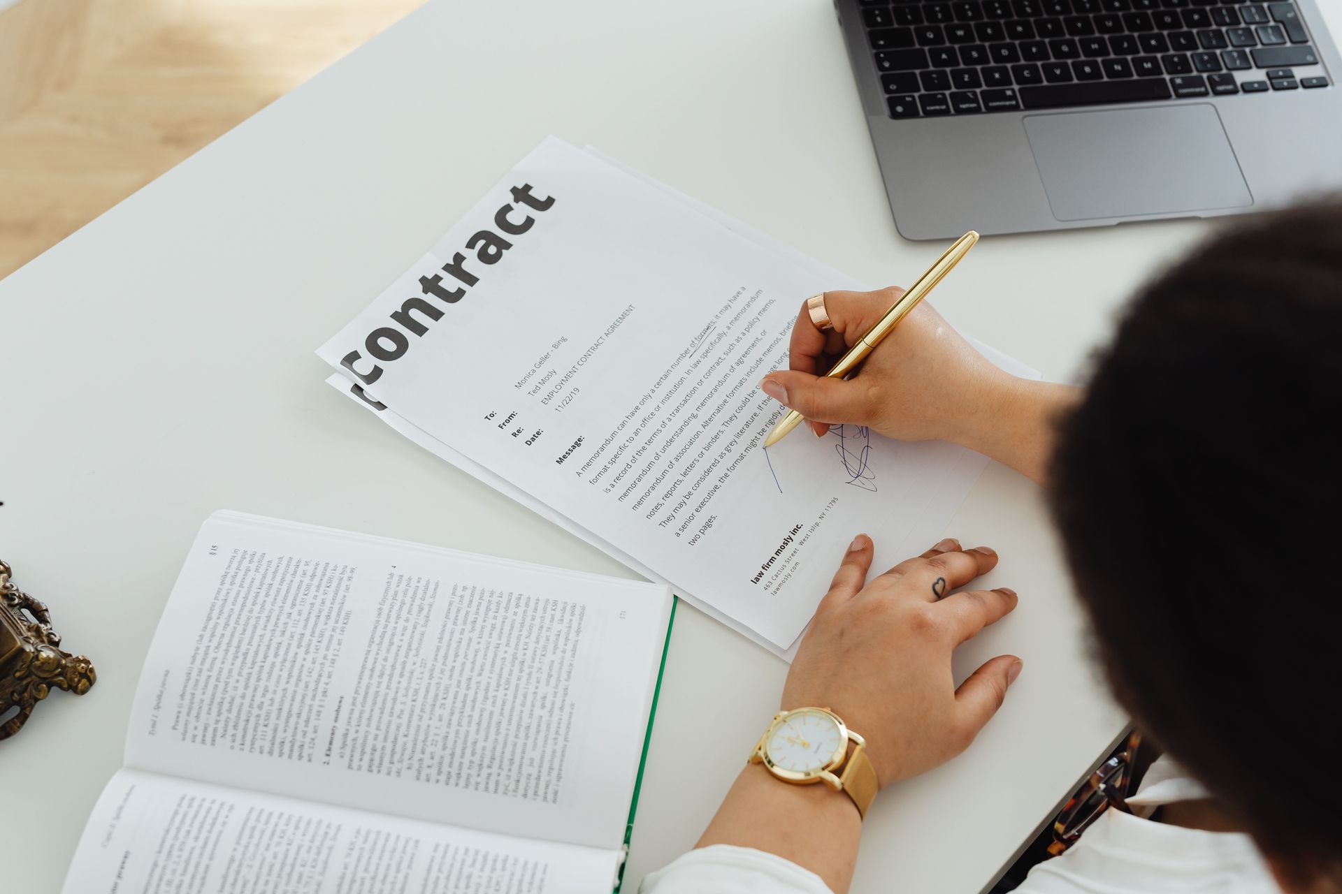 Person signing a contract at a desk with documents and a laptop nearby