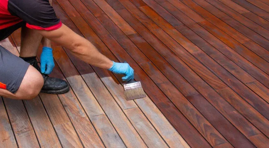Person wearing blue gloves applying finish to a wooden deck with a brush