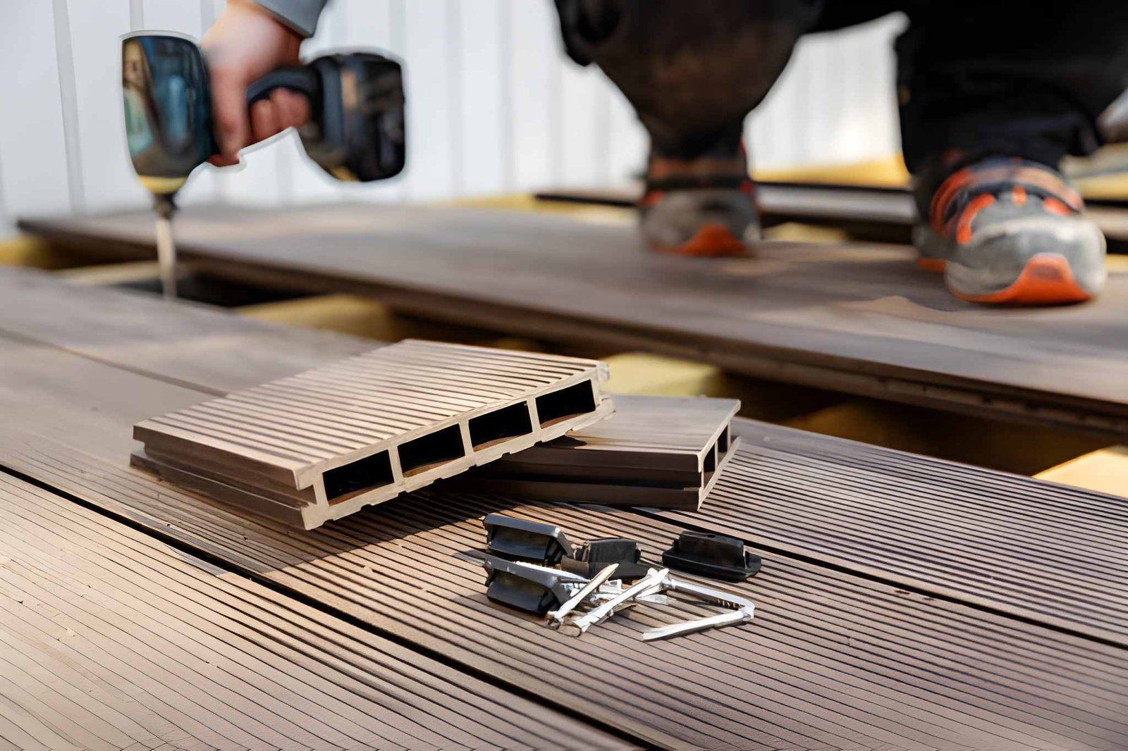Hands using a drill on a wooden deck with composite boards and screws nearby