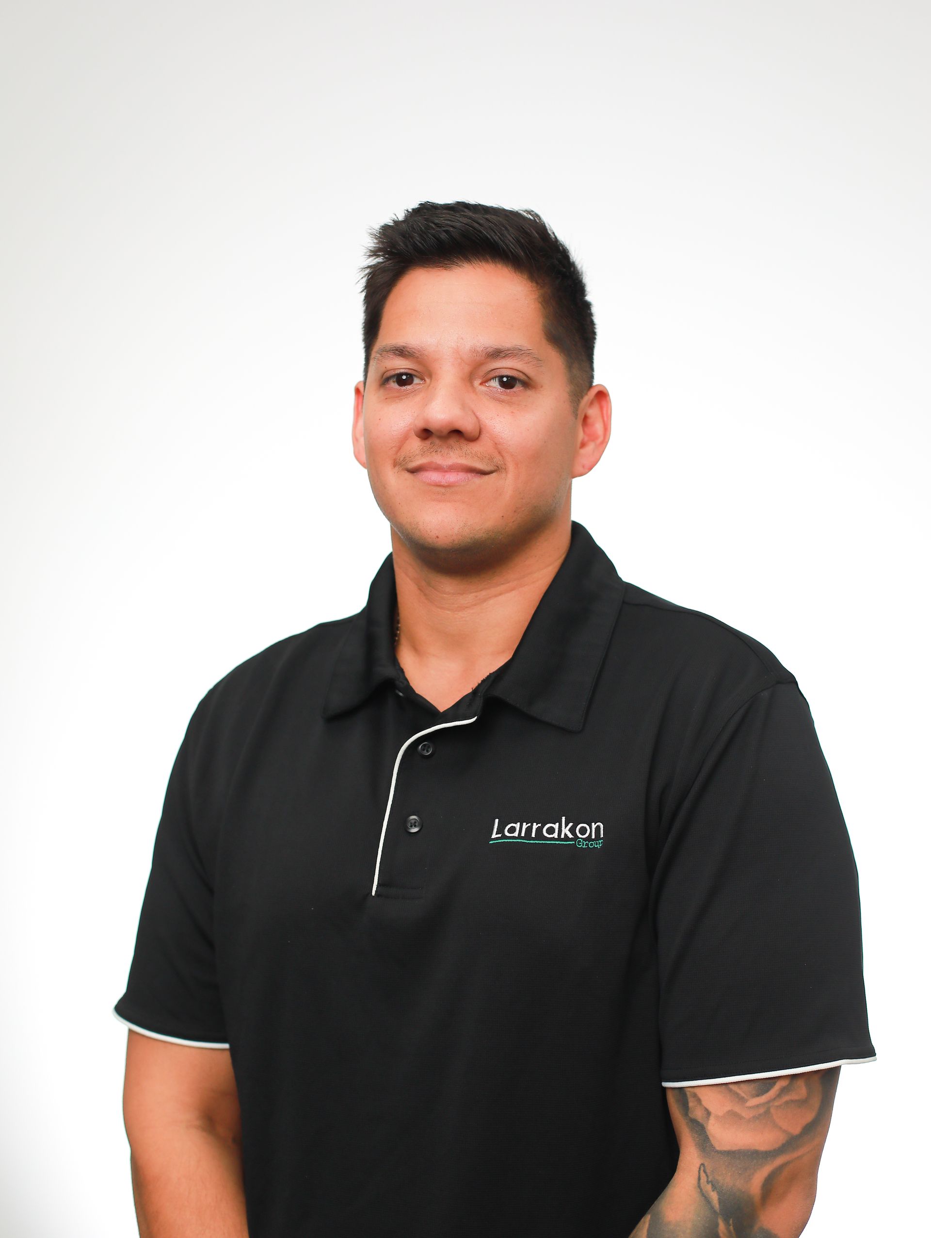 A man with a tattoo on his arm is wearing a black polo shirt.