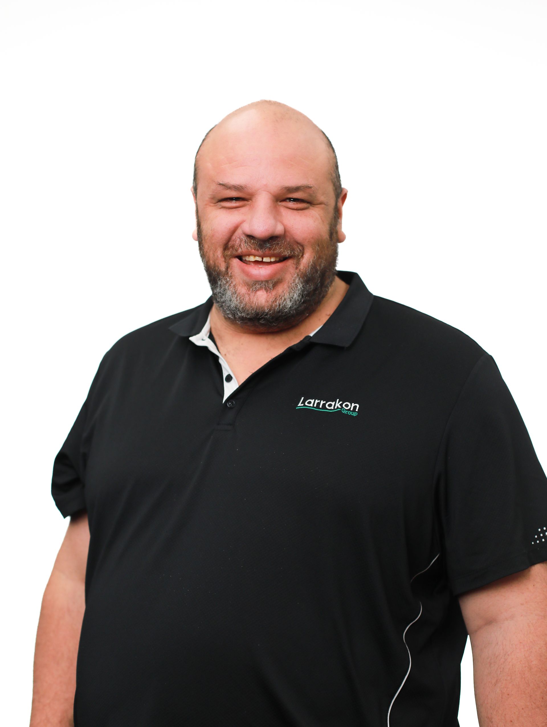 A bald man with a beard is wearing a black polo shirt and smiling.