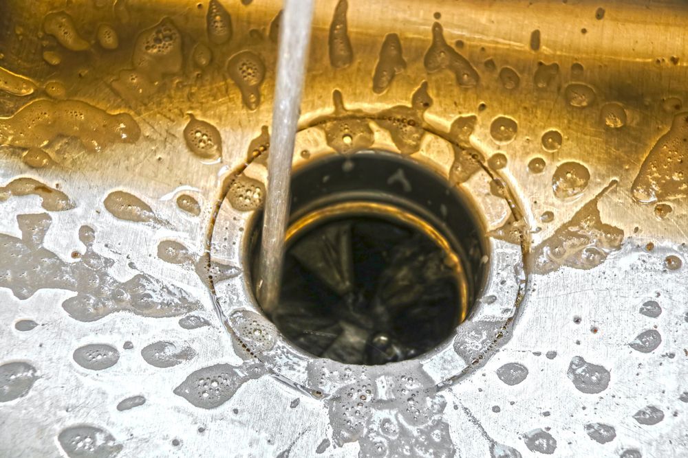 Water pouring into a stainless steel sink drain with soap bubbles around it