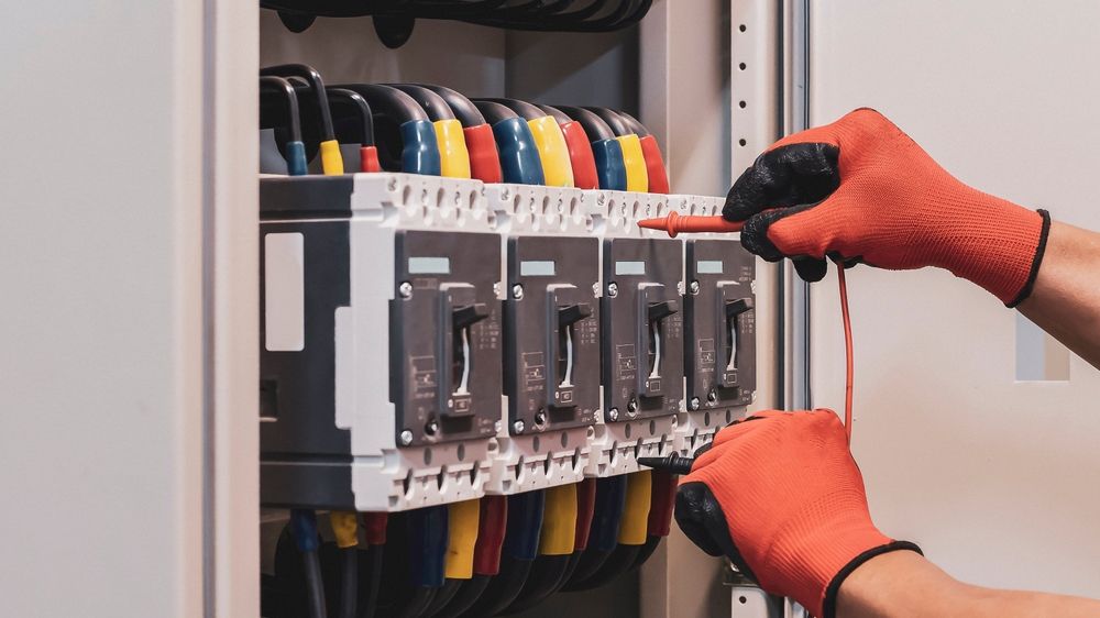 Gloved hands wiring an electrical breaker panel with colored cables