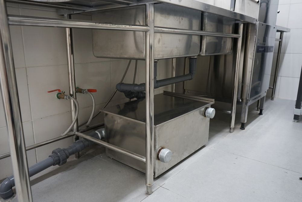 Stainless steel industrial equipment and piping beneath a metal worktable in a clean room