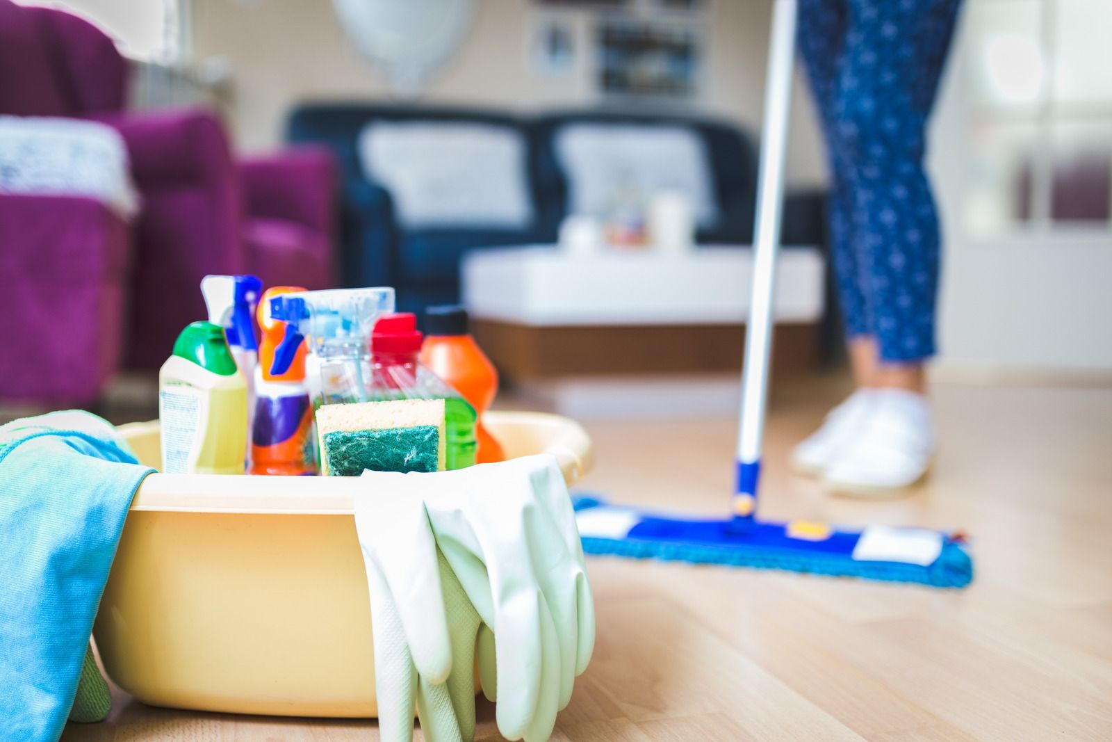 A person mops a wooden floor in a living room; a bucket of cleaning supplies sits nearby.