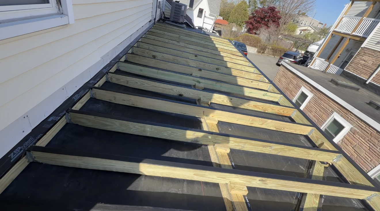 Roof under repair with black waterproofing and wooden battens beside a house exterior
