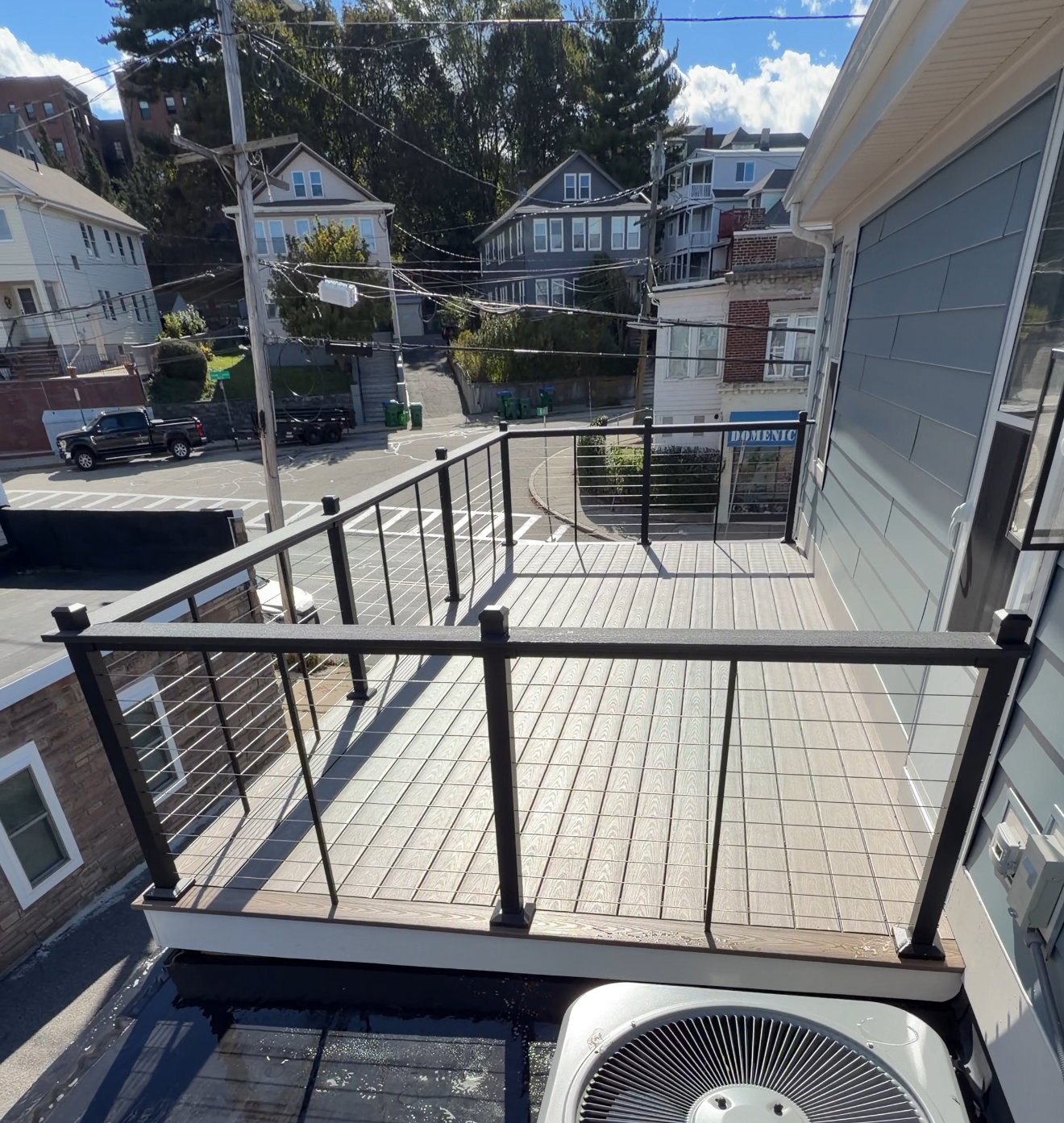 Small rooftop deck with black railing, brick pavers, and a view of houses across the street.