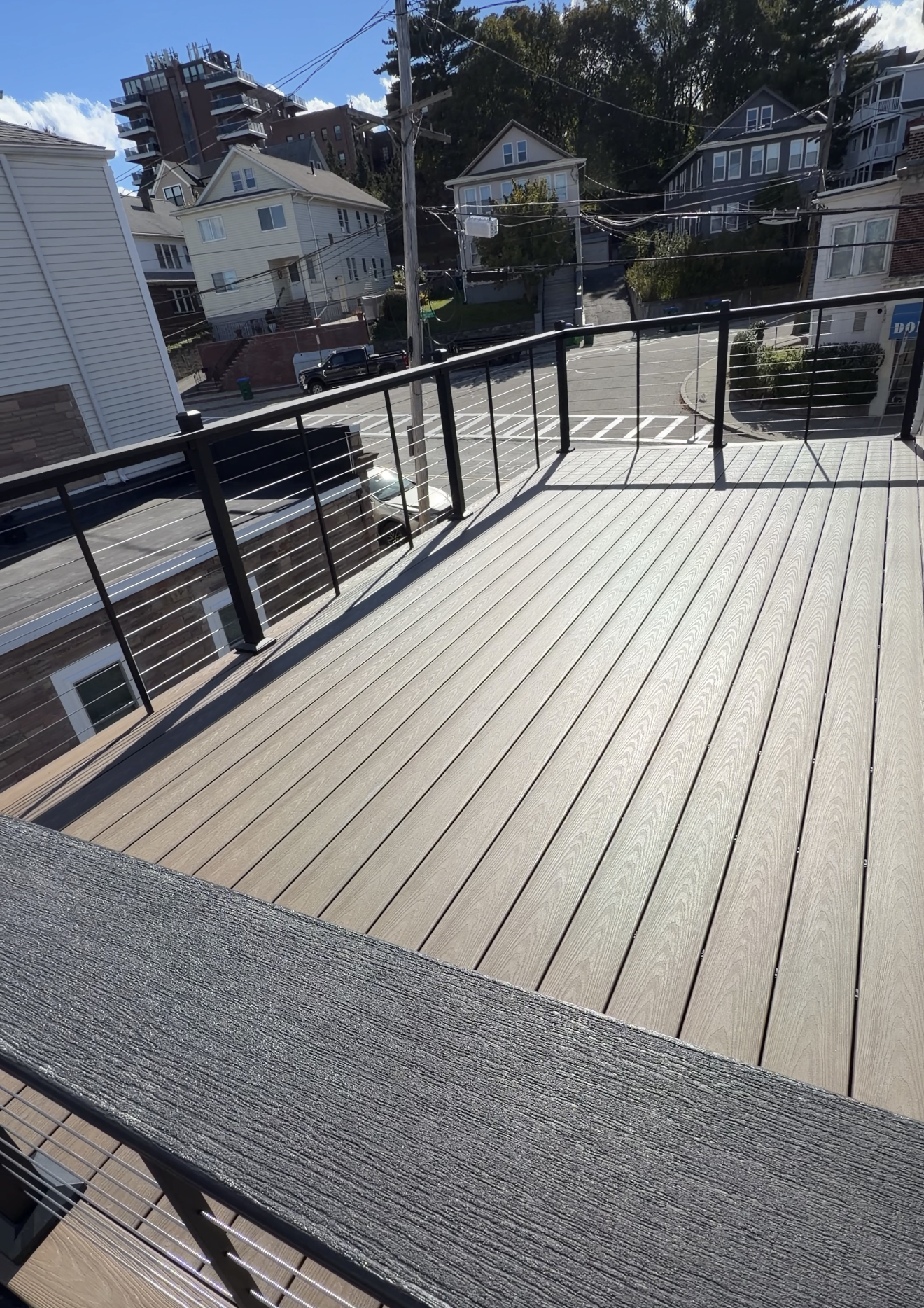 Wooden rooftop deck with black railings and neighboring houses in sunlight