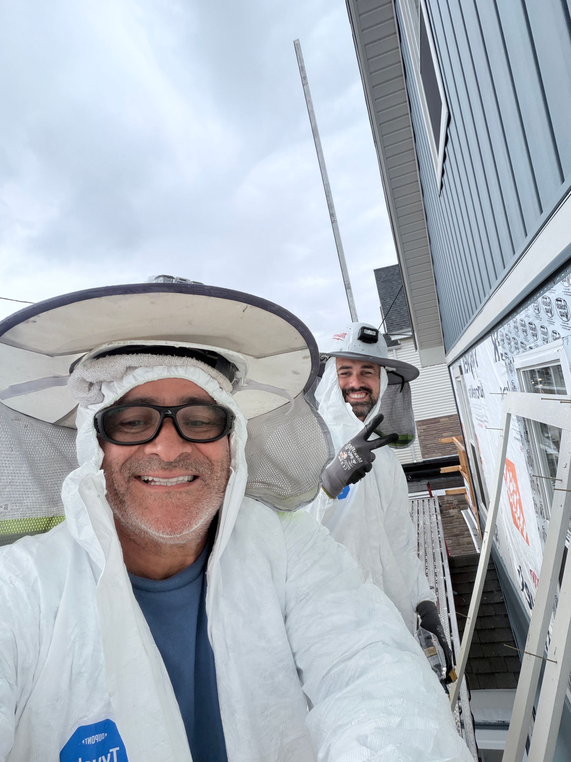 Two smiling people in white rain ponchos on a boat deck, one wearing a wide-brimmed hat.