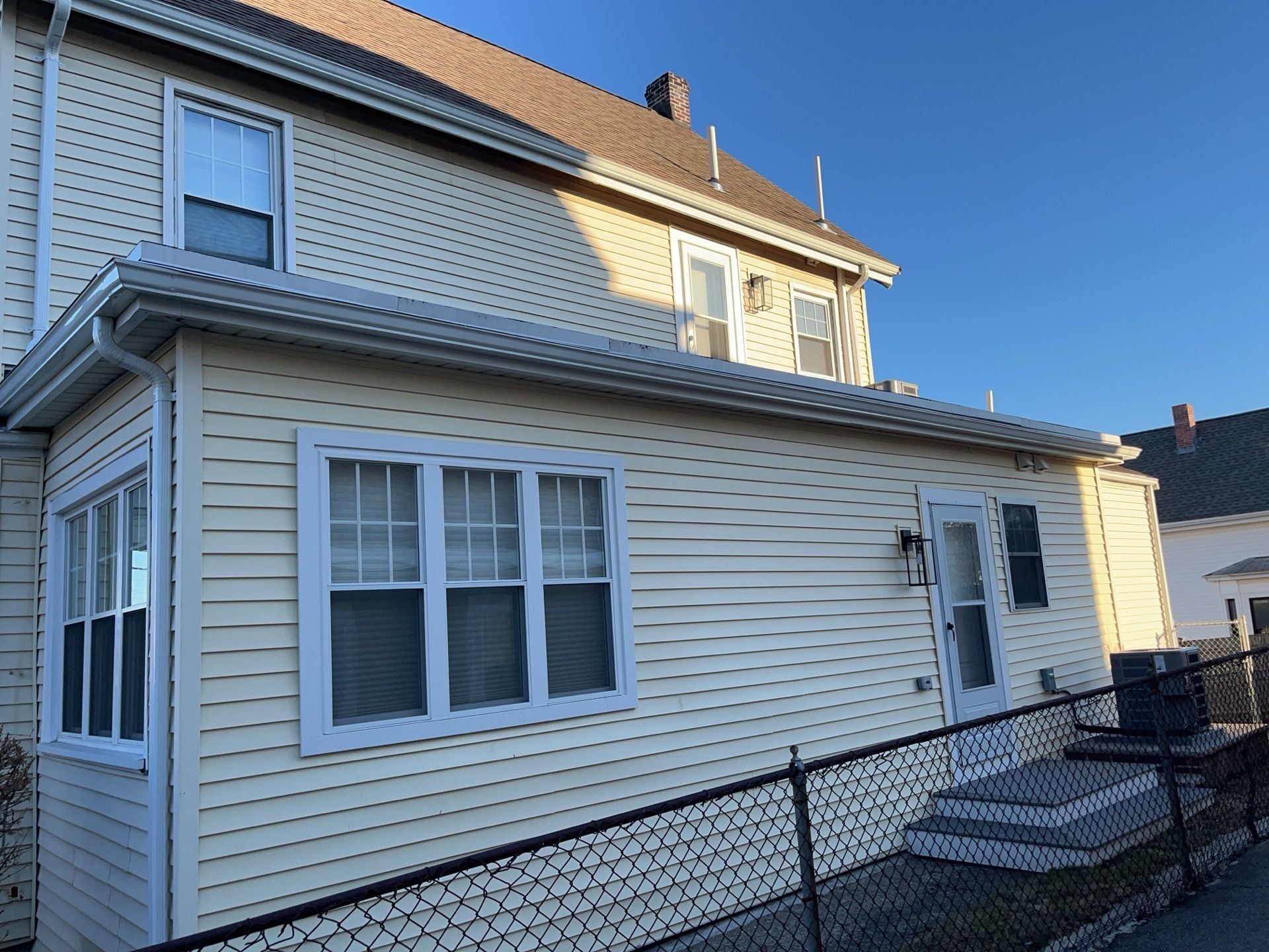 Side view of a light blue house with white siding, windows, a small porch, and a chain-link fence