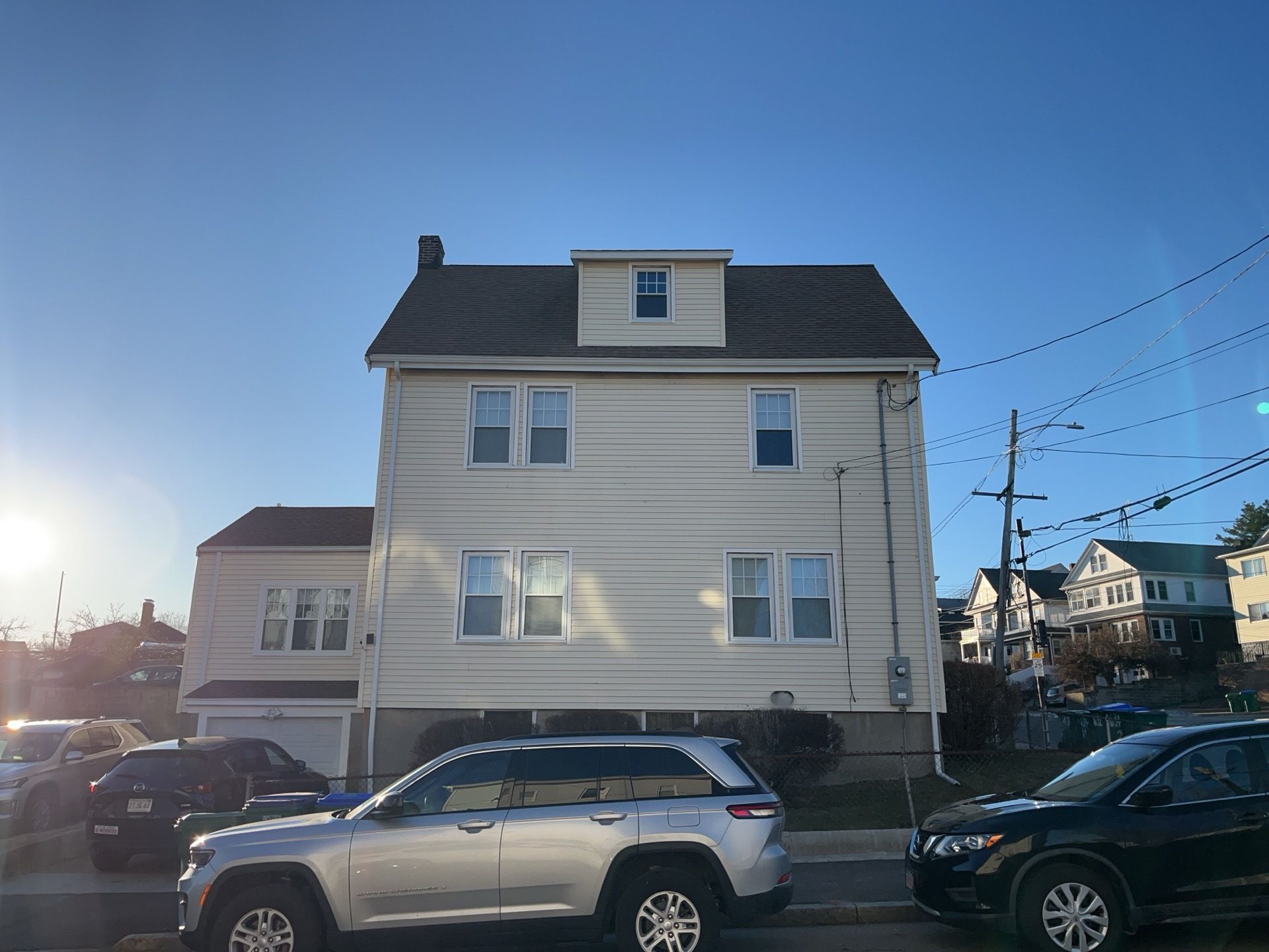 White multi-story house with parked cars in front on a sunny street corner.