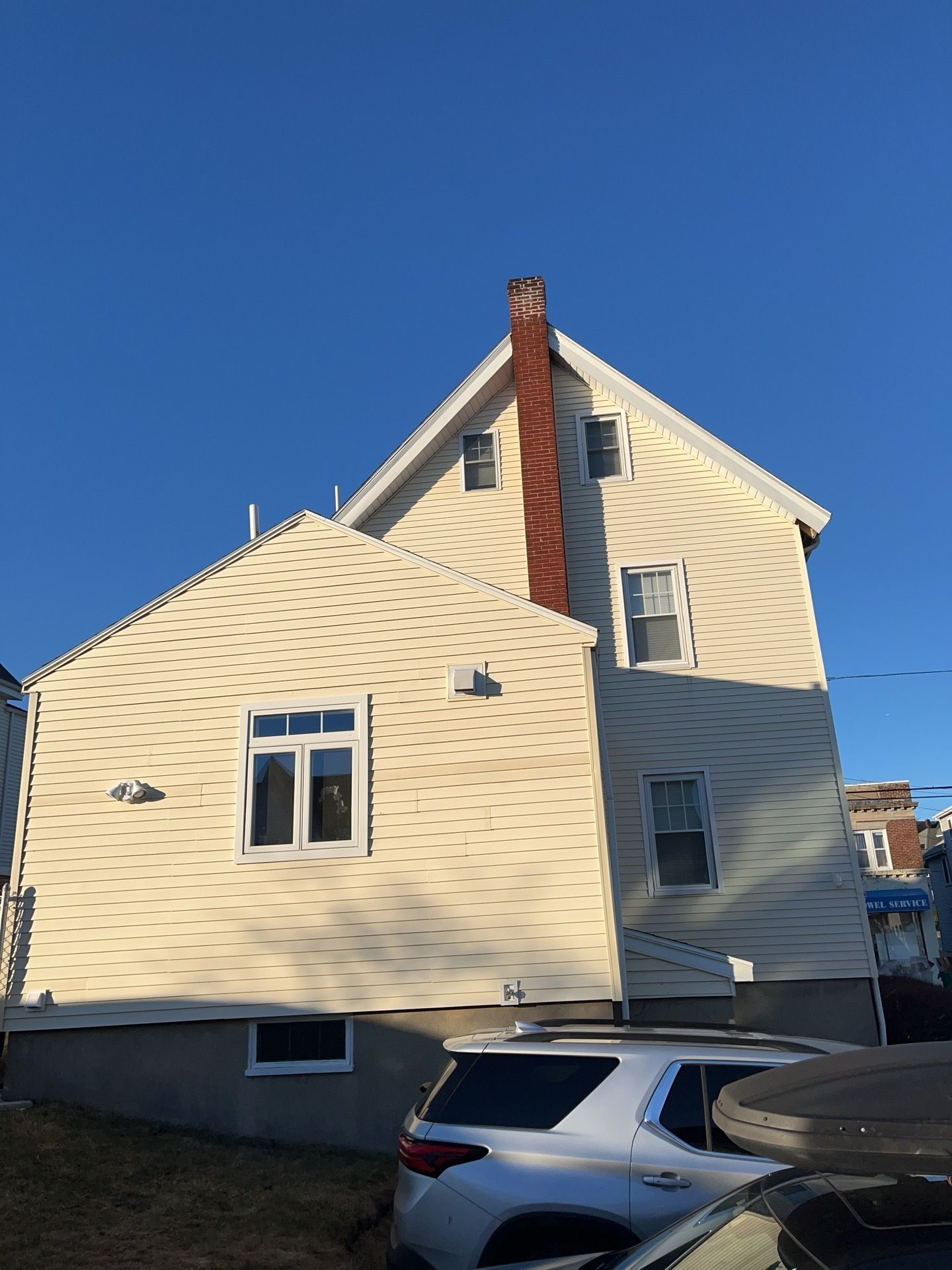 White-sided house with a red chimney and parked SUV under a clear blue sky