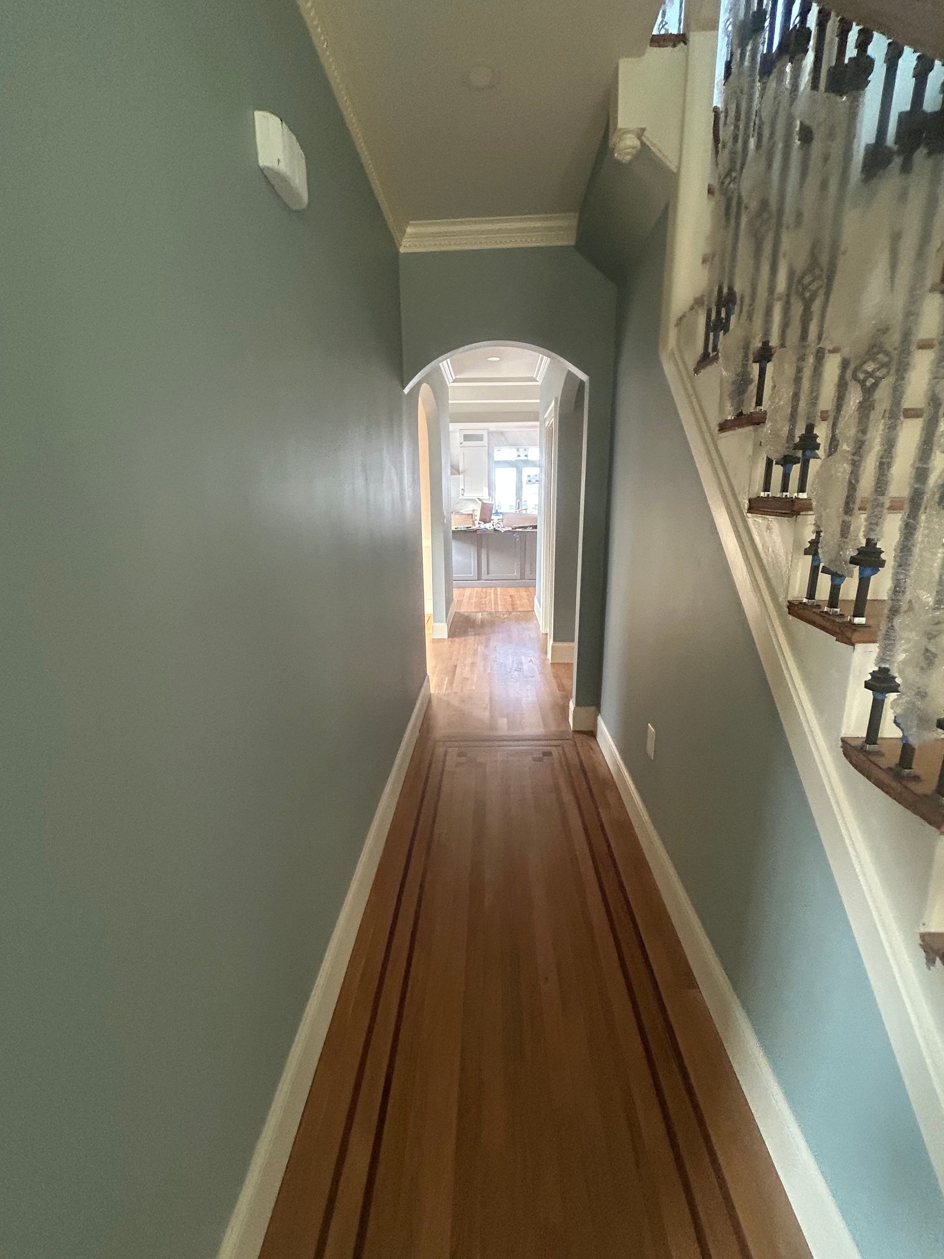 Narrow hallway with teal walls, wood floor runner, and staircase railing on the right.