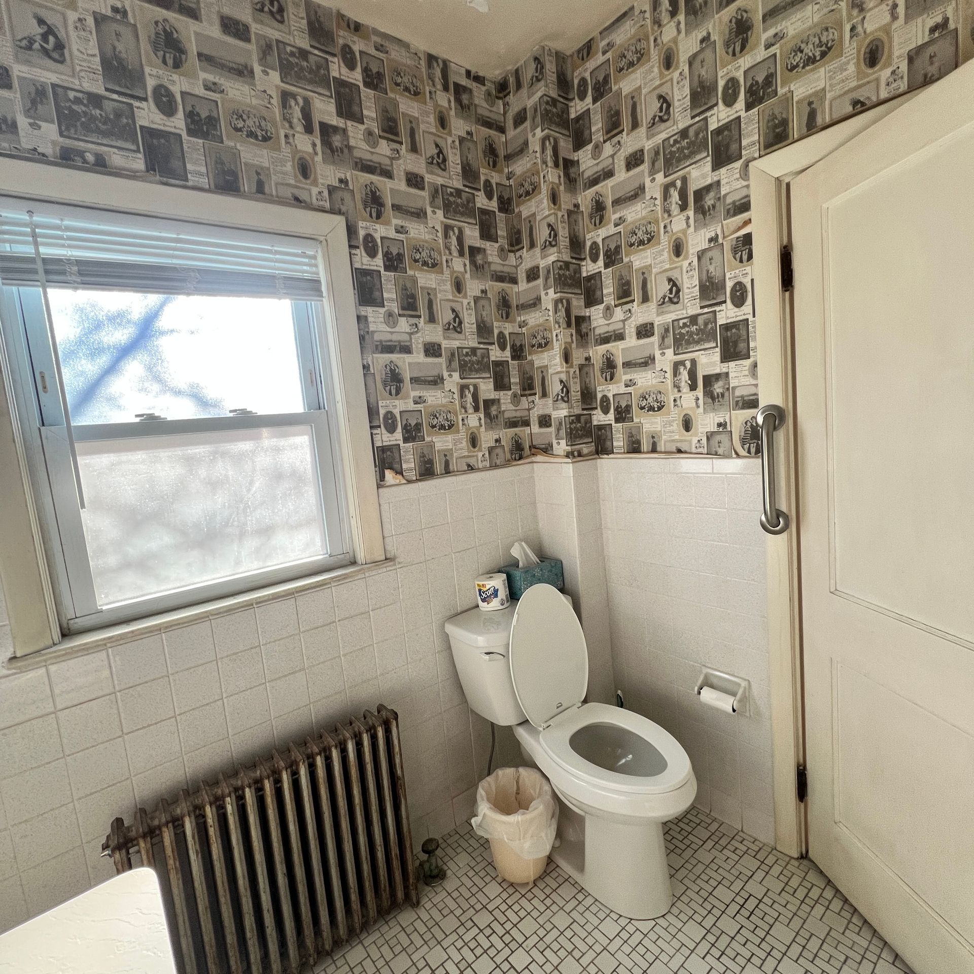 Small bathroom with toilet, radiator, window, patterned wallpaper, and closed door.