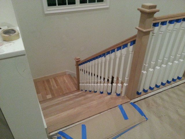 Stair landing with white balusters and blue-taped floor markings near a doorway