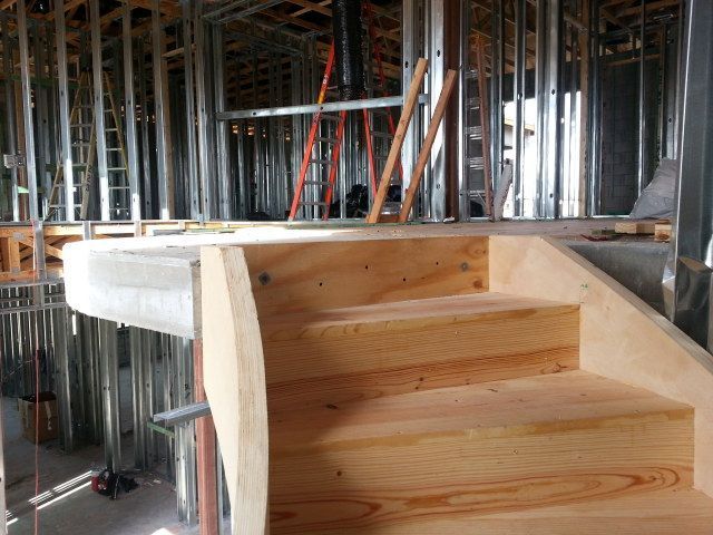 Unfinished wooden staircase under construction in a building with exposed framing and tools in the background