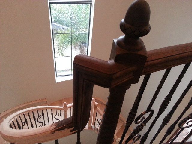 View down a wooden staircase with ornate spindles and a curved railing beside a window.