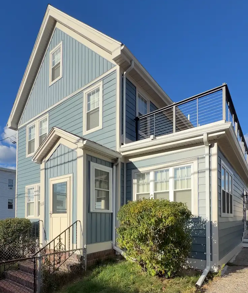 Blue two-story house with white trim, front steps, and a small upper deck under a clear sky