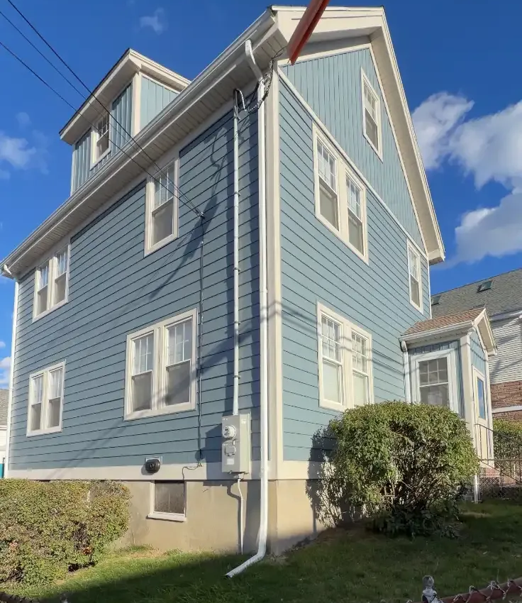 Blue two-story house with white trim, dormer windows, and a small front lawn under a bright sky