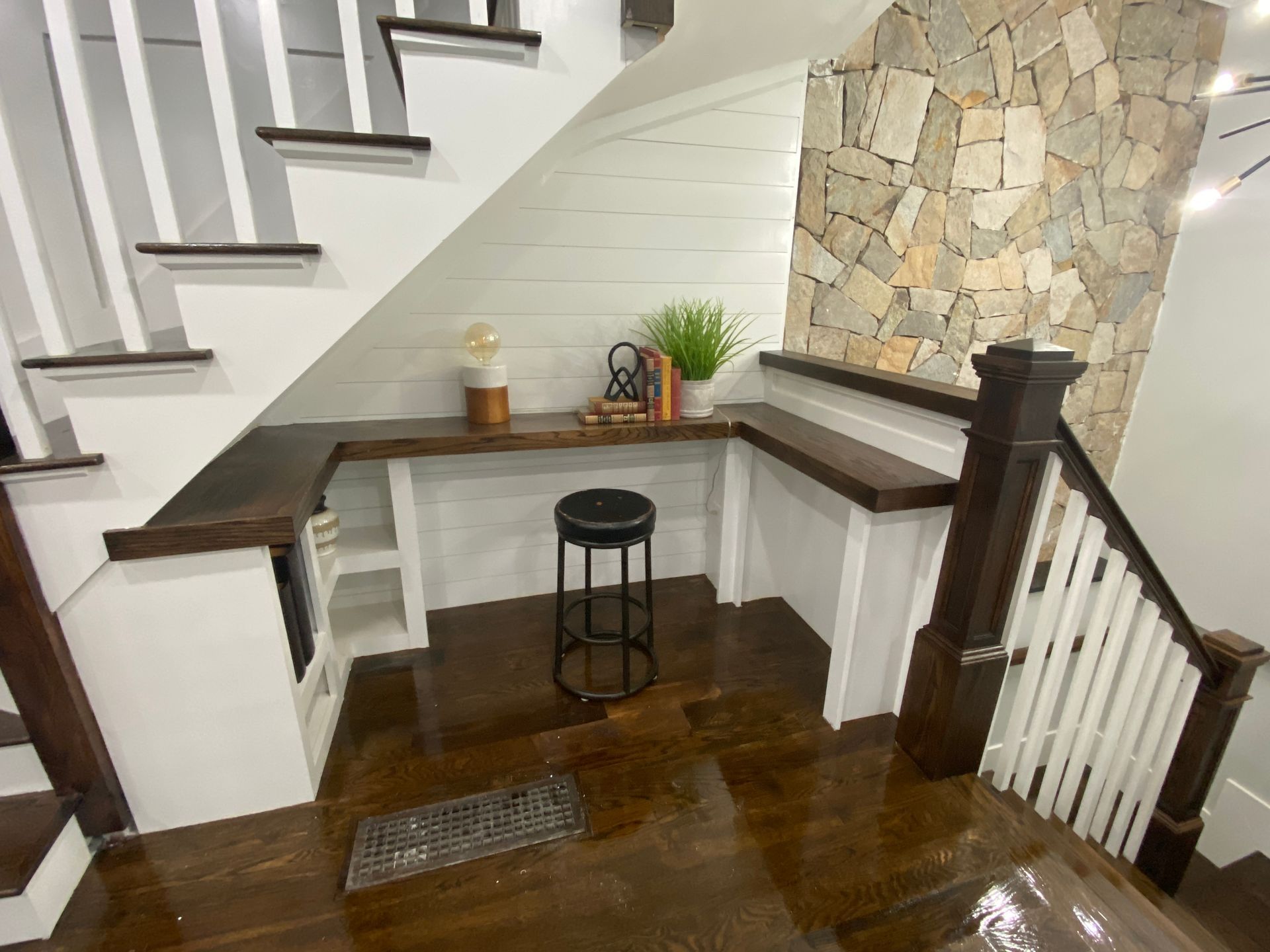 Small stair landing with dark wood desk, stool, white walls, and stone accent wall.